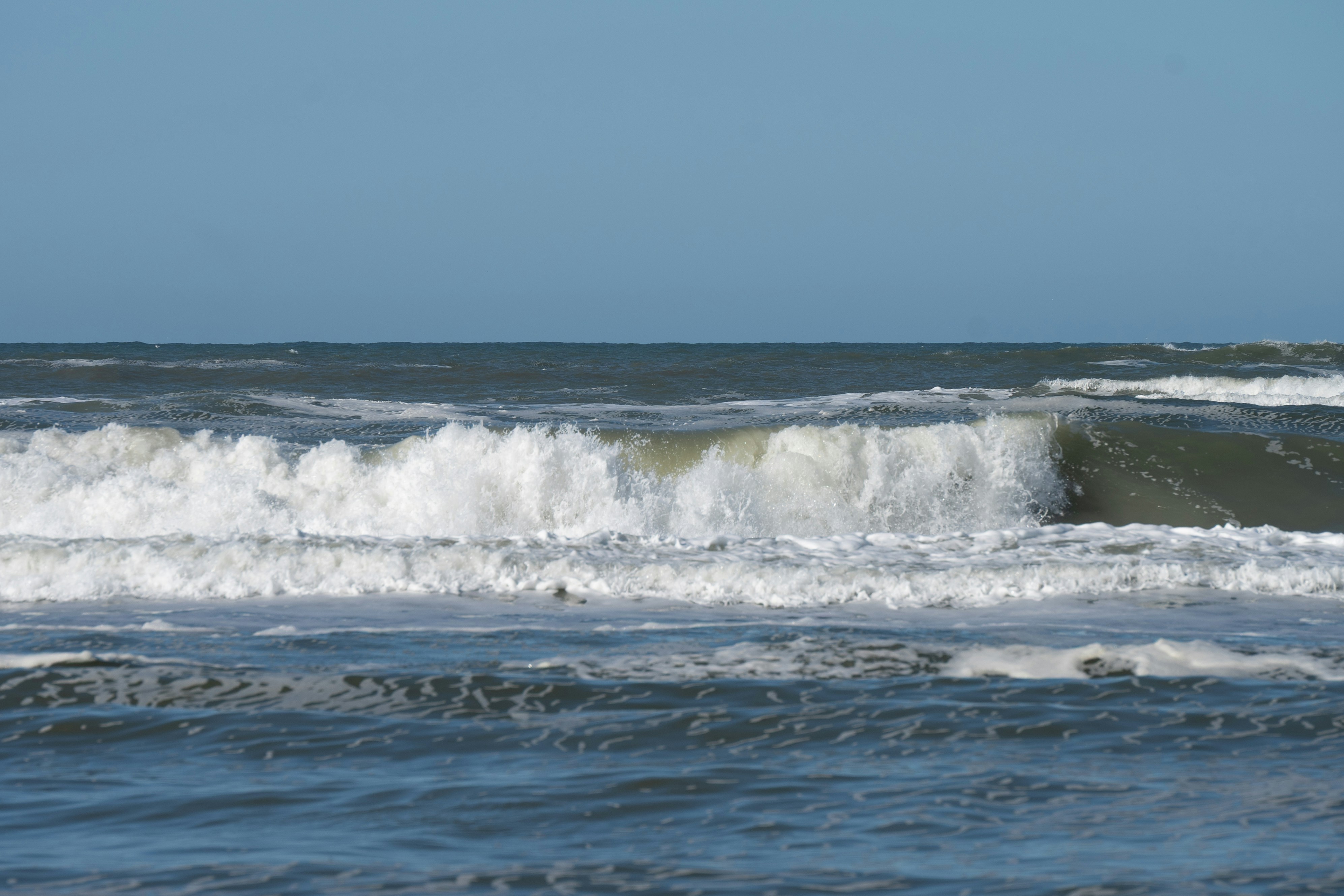 Ocean waves crashing under a clear blue sky
