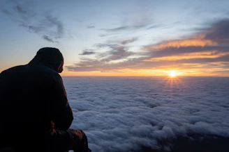 Man sitting above clouds watching the sunset
