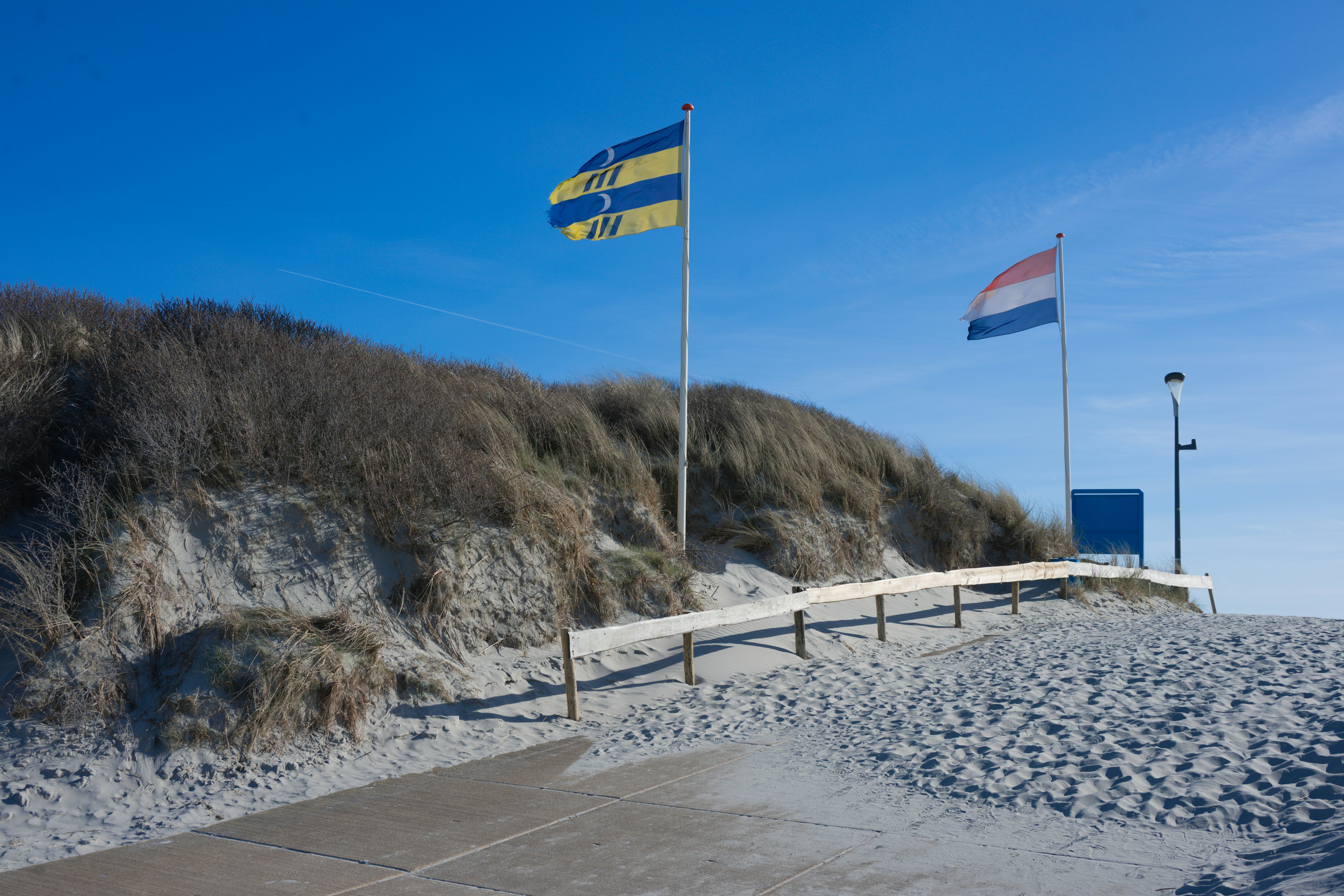 Deux drapeaux flottent au-dessus des dunes de sable par temps clair.