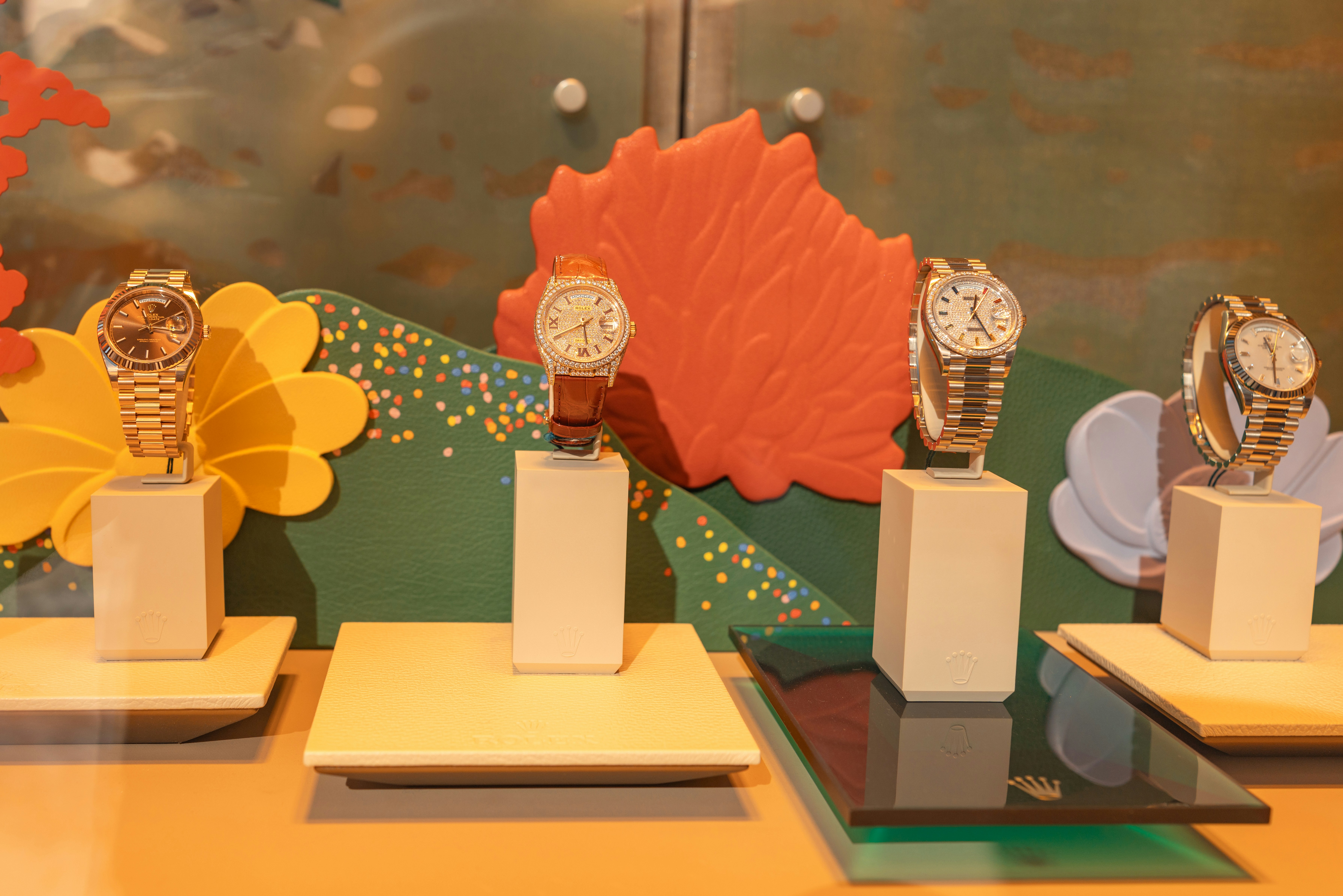 Four watches displayed on stands with decorative background.