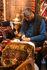 Man sewing fringes onto a colorful oriental rug.