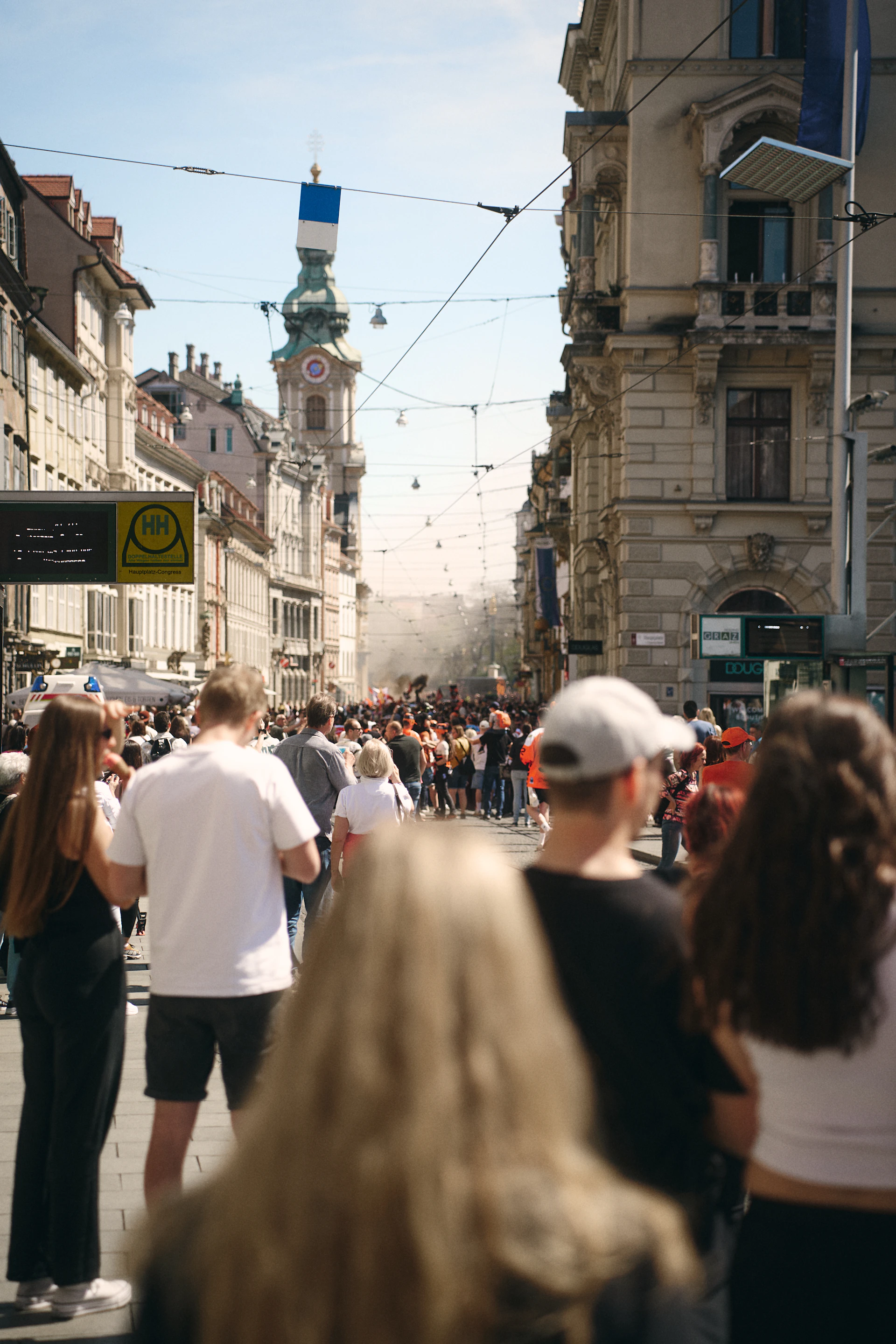 Crowd gathered on a city street with buildings and tower.