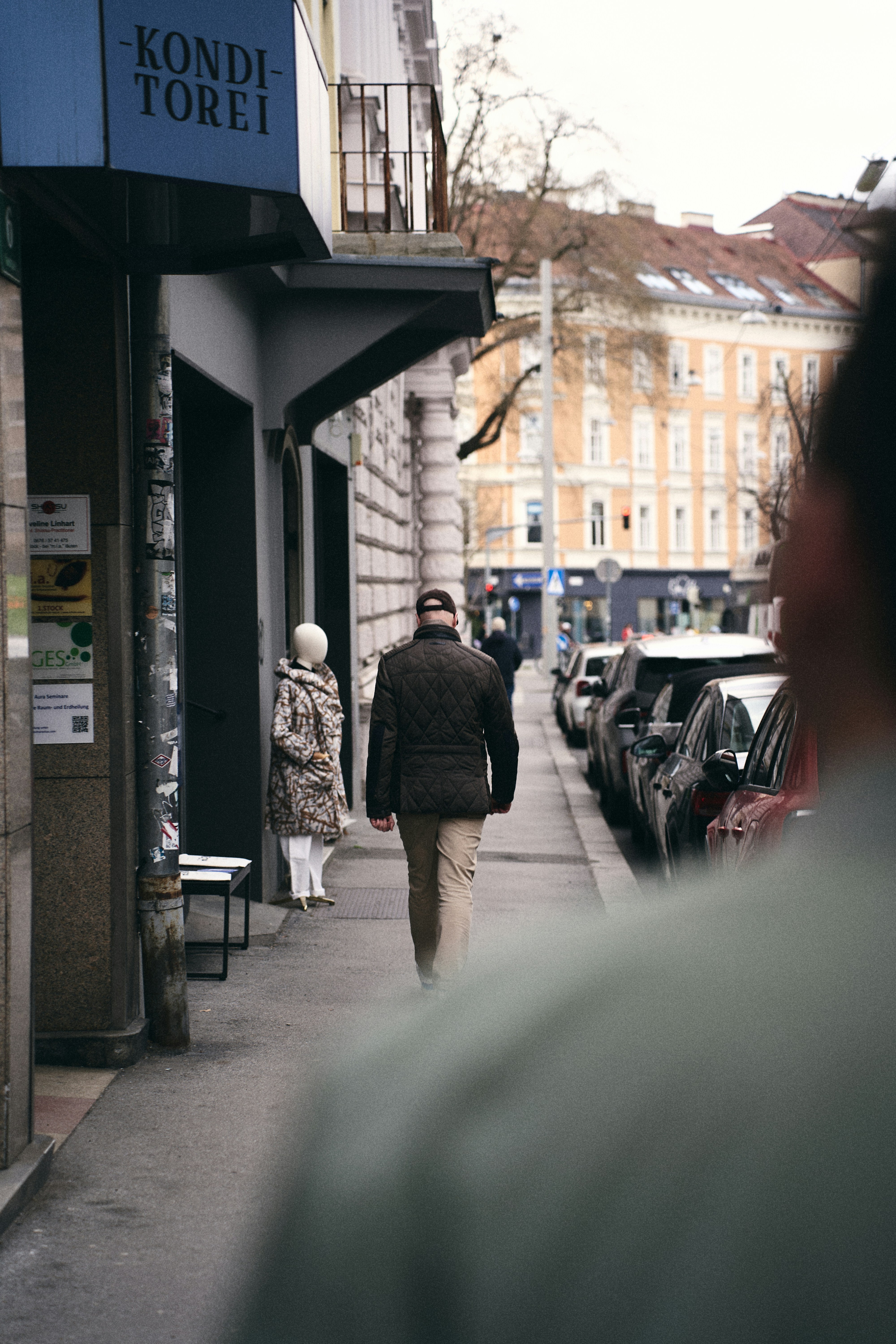 Man walks down a city street past a shop window.