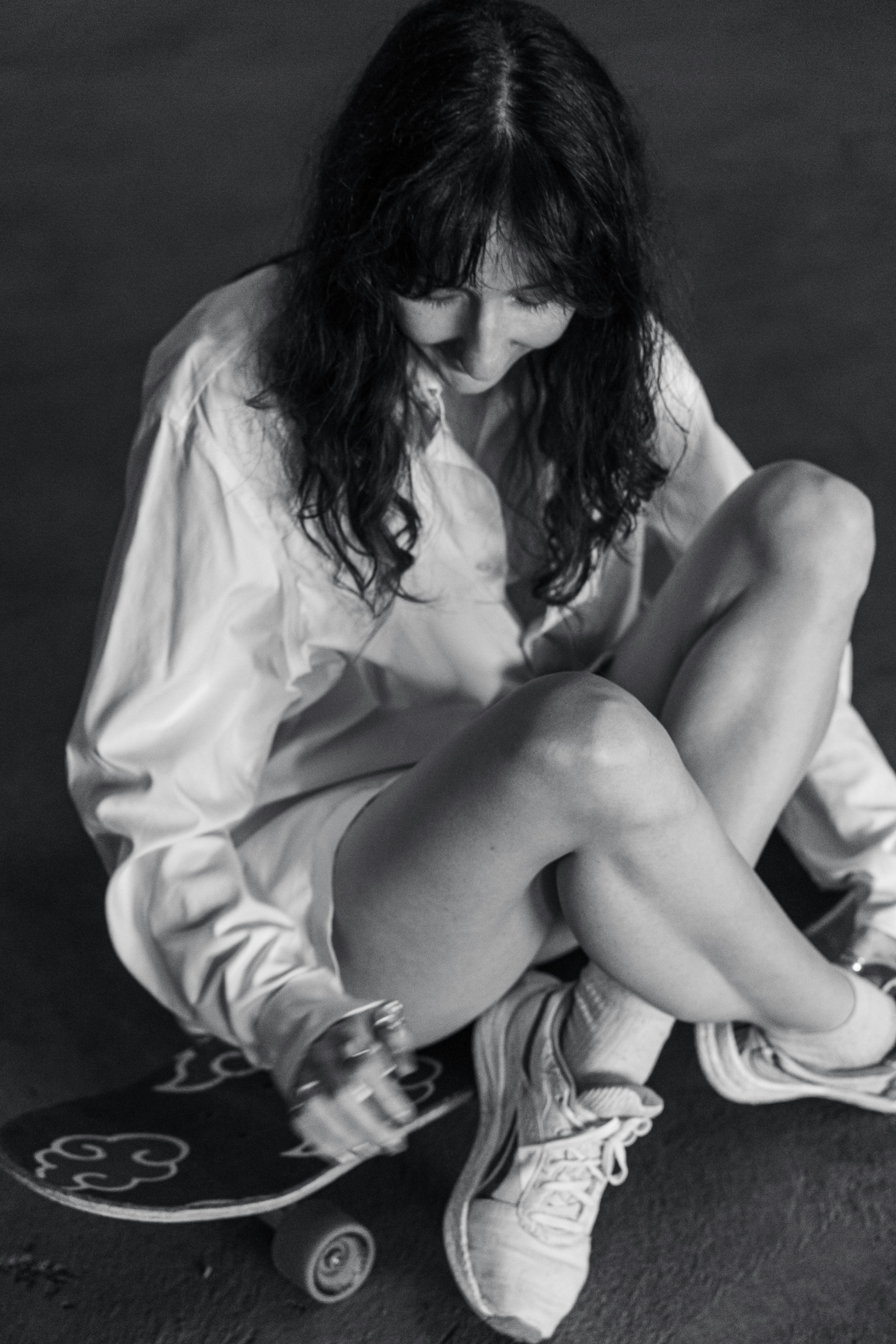 Femme en chemise blanche assise sur un skateboard.