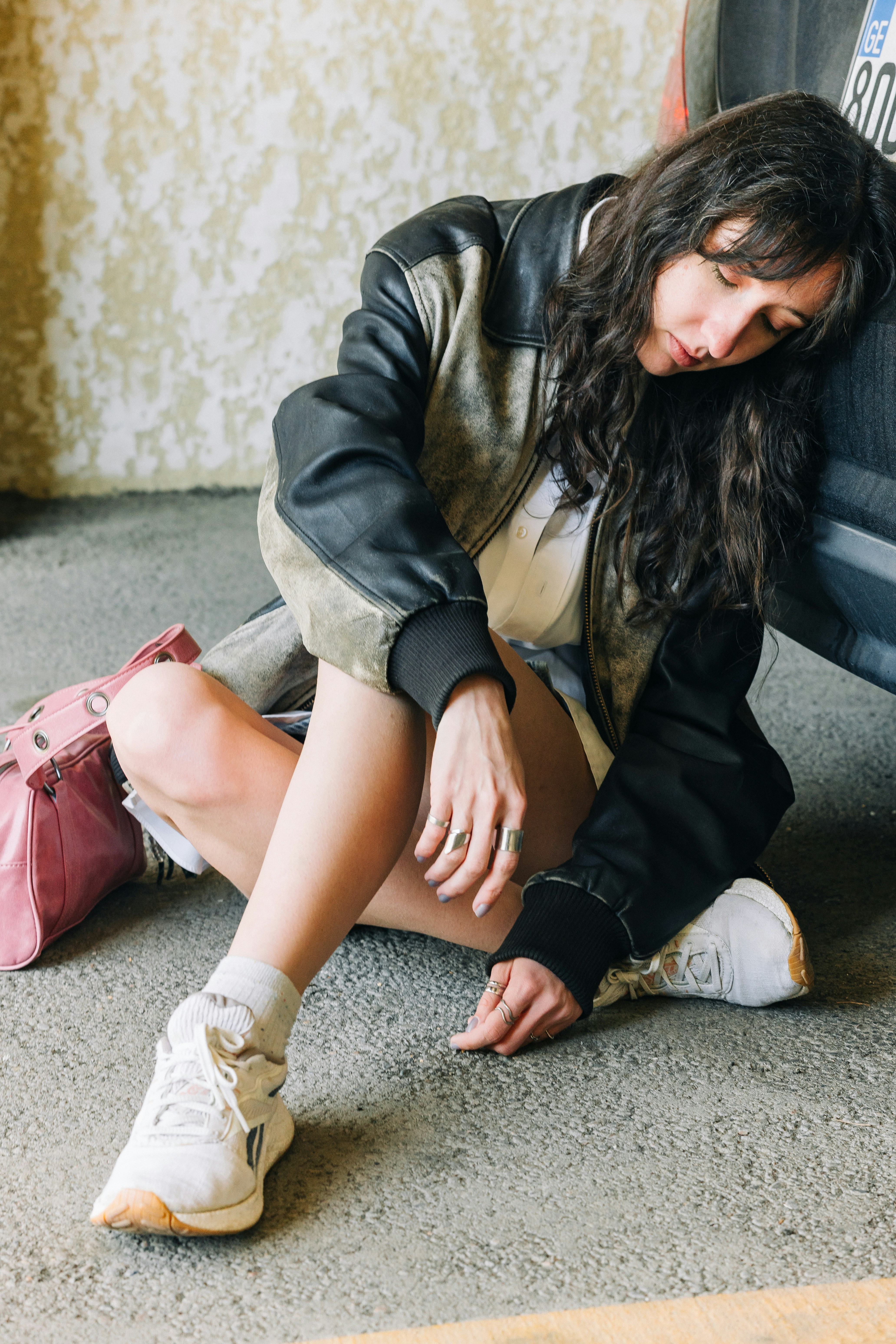 Femme appuyée contre un véhicule avec un sac rose.
