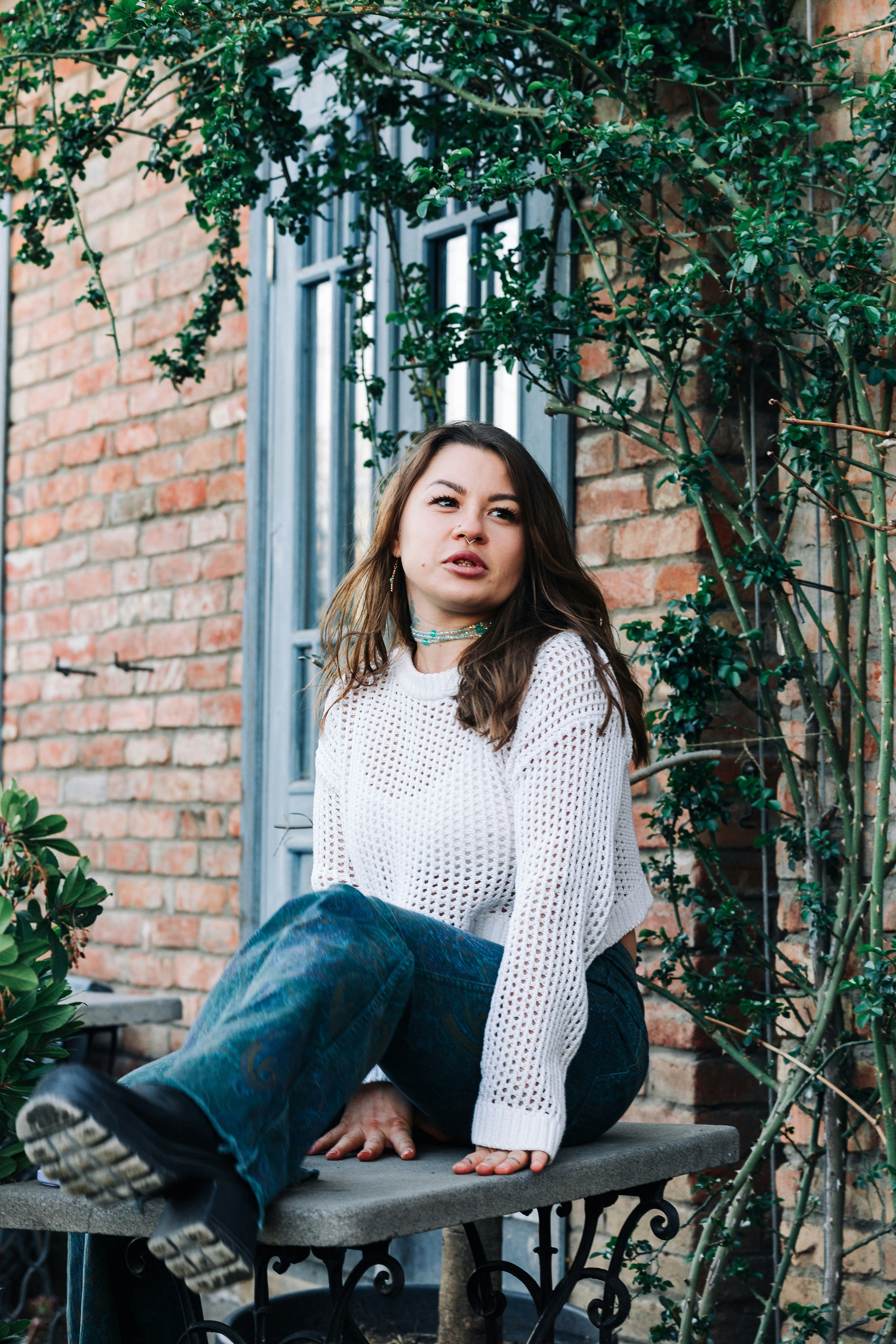 Jeune femme en pull blanc et jean assise dehors