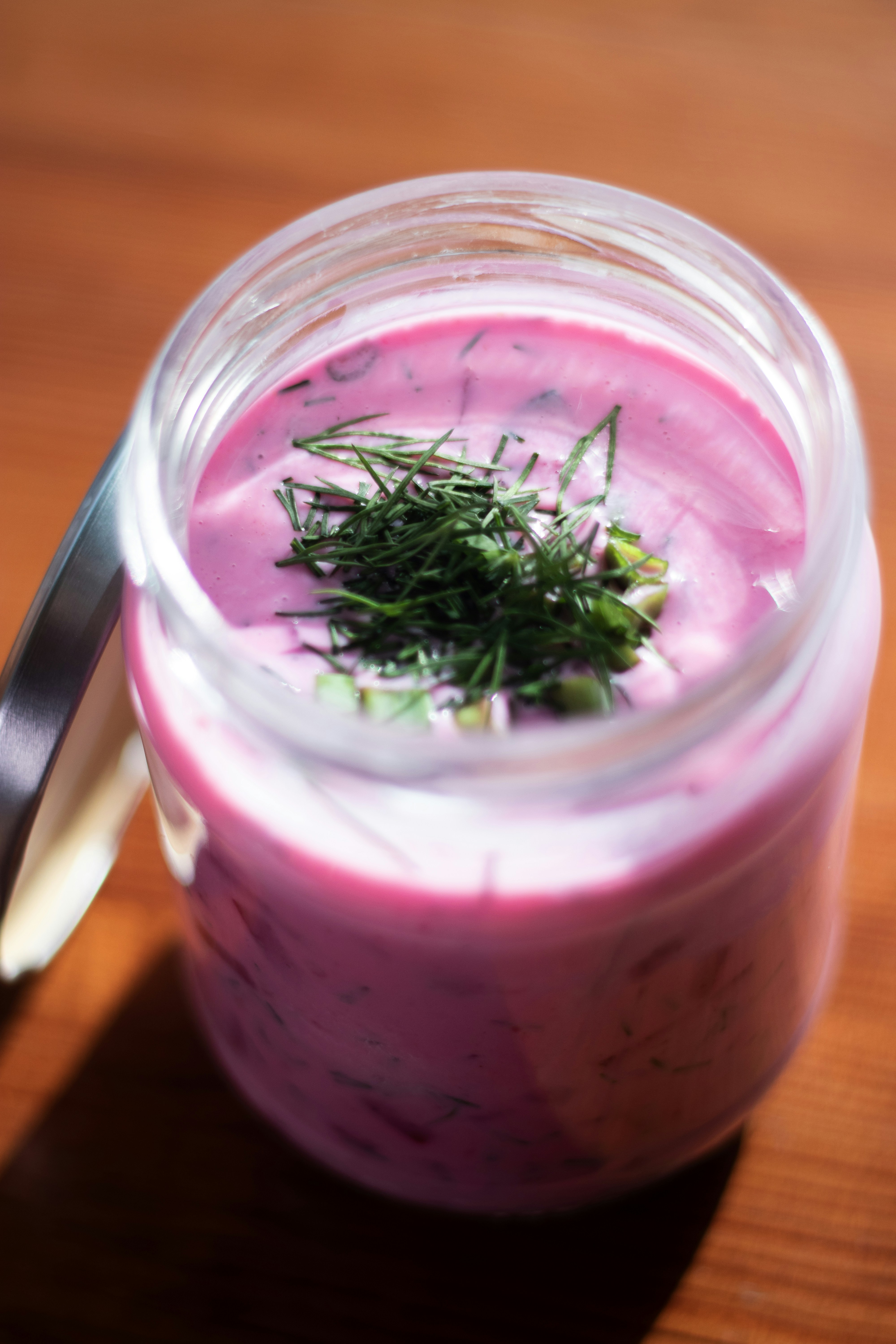 Un barattolo di zuppa rosa con aneto e cipollotti.