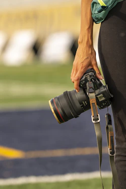 A person holds a professional camera on a sports field.