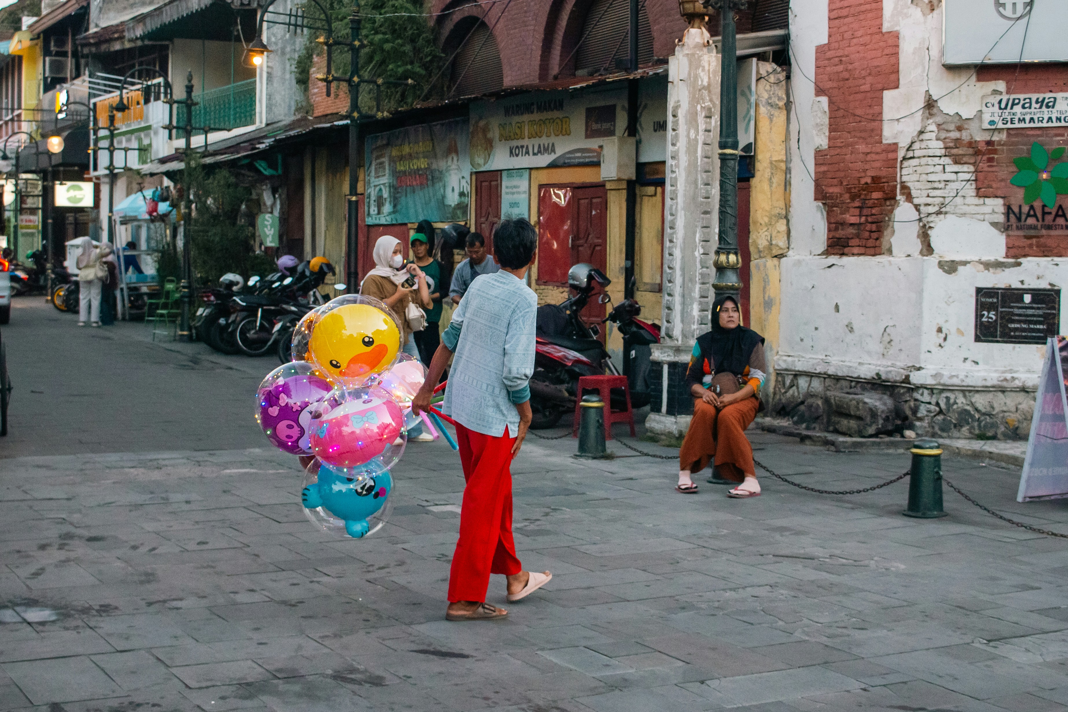 Man carrying colorful balloons down a street.