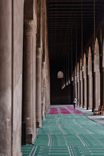 Person walks down a long hallway with arched columns.