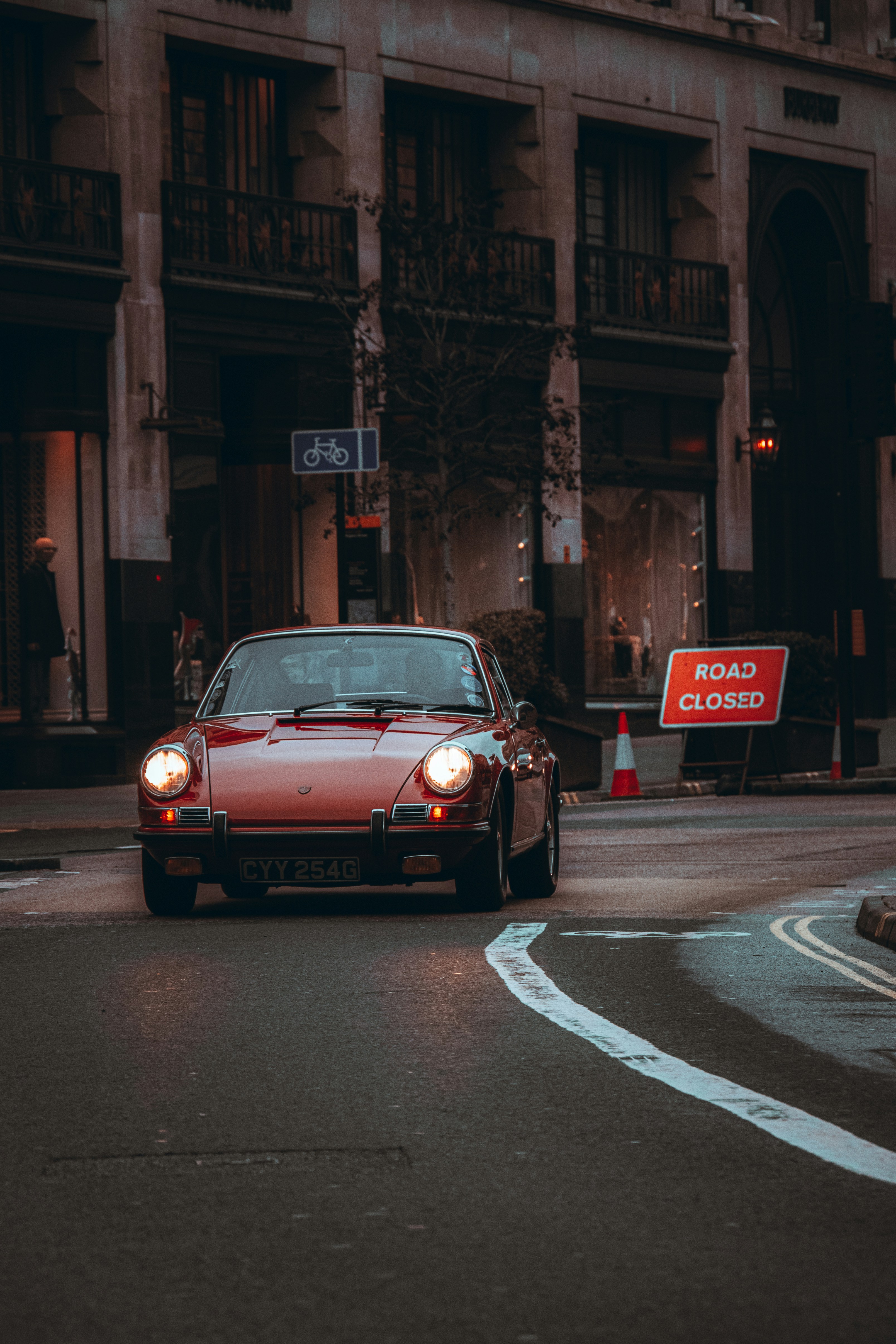 A red vintage car driving on a city street.