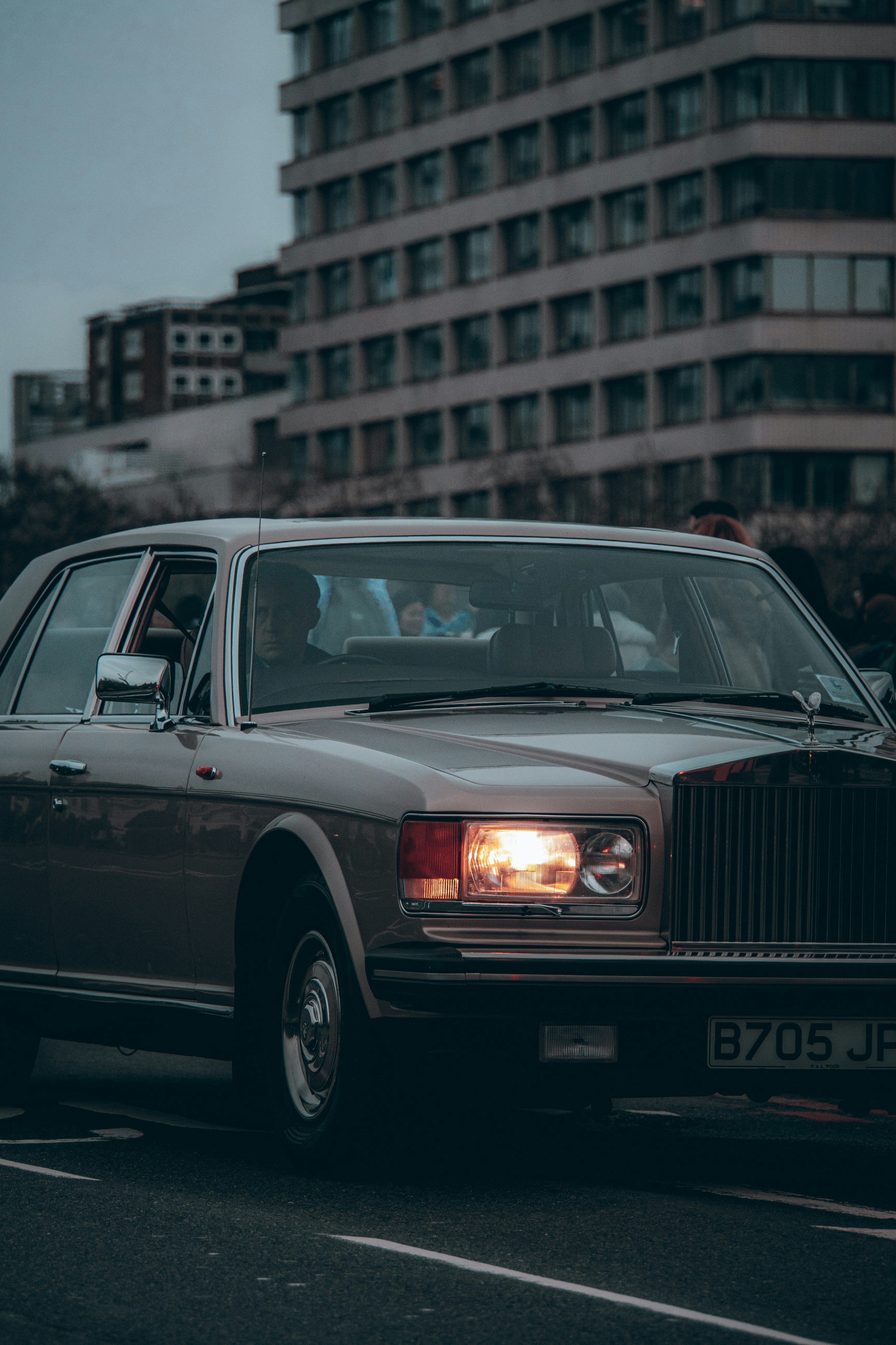 A vintage luxury car drives past a modern building.