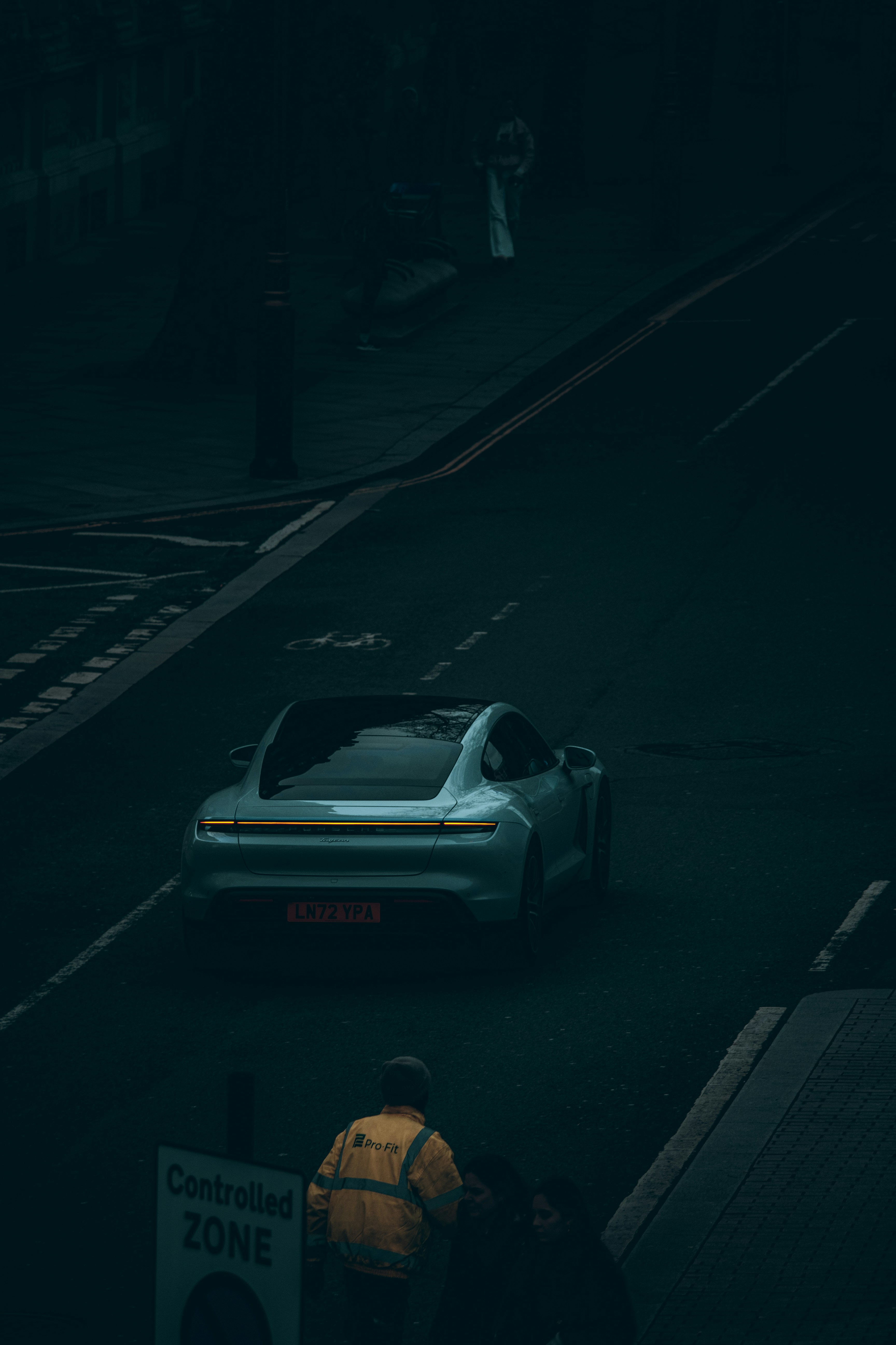 A light blue car drives down a dark street.