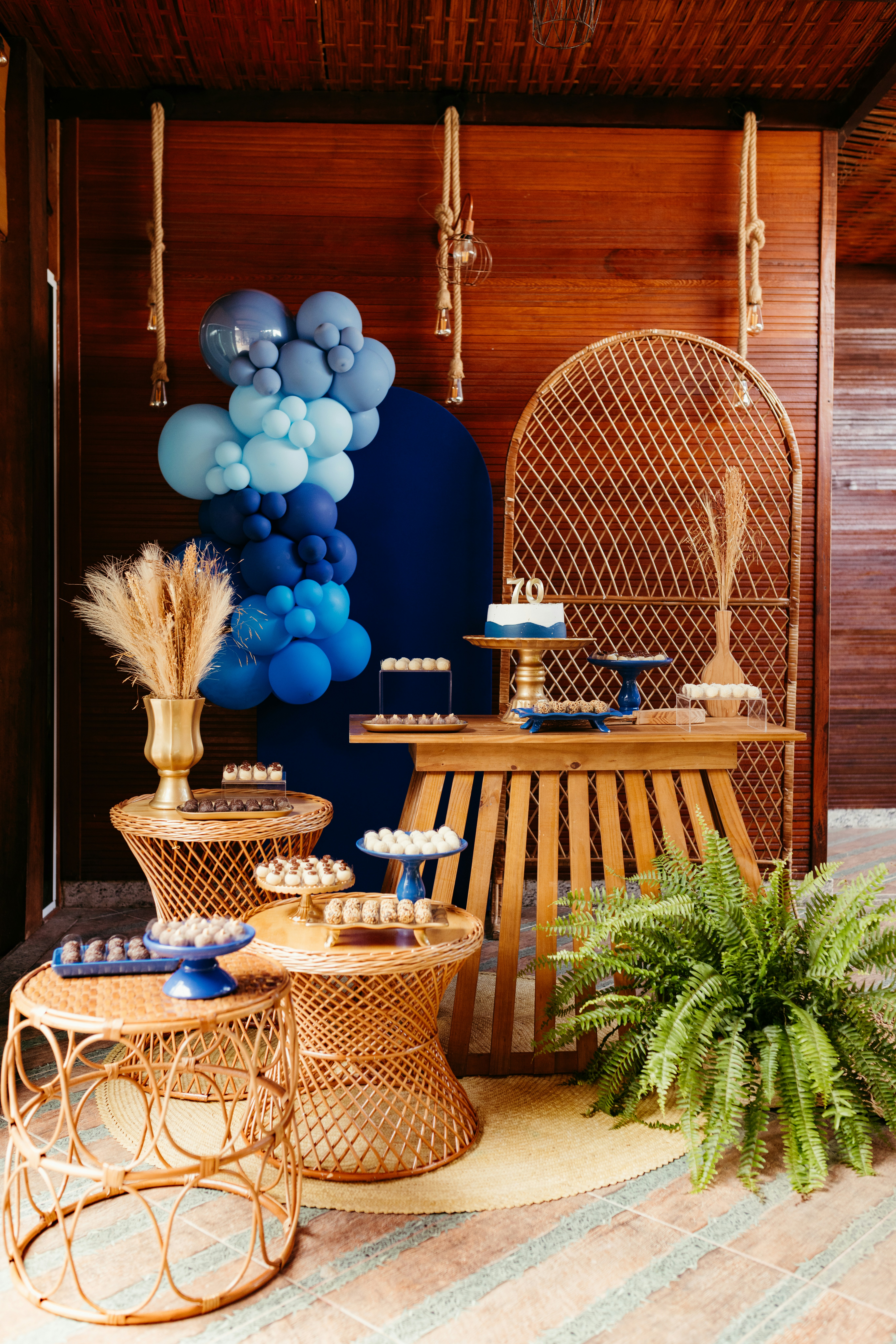 Birthday dessert table decorated with blue balloons, greenery and coordinated party details