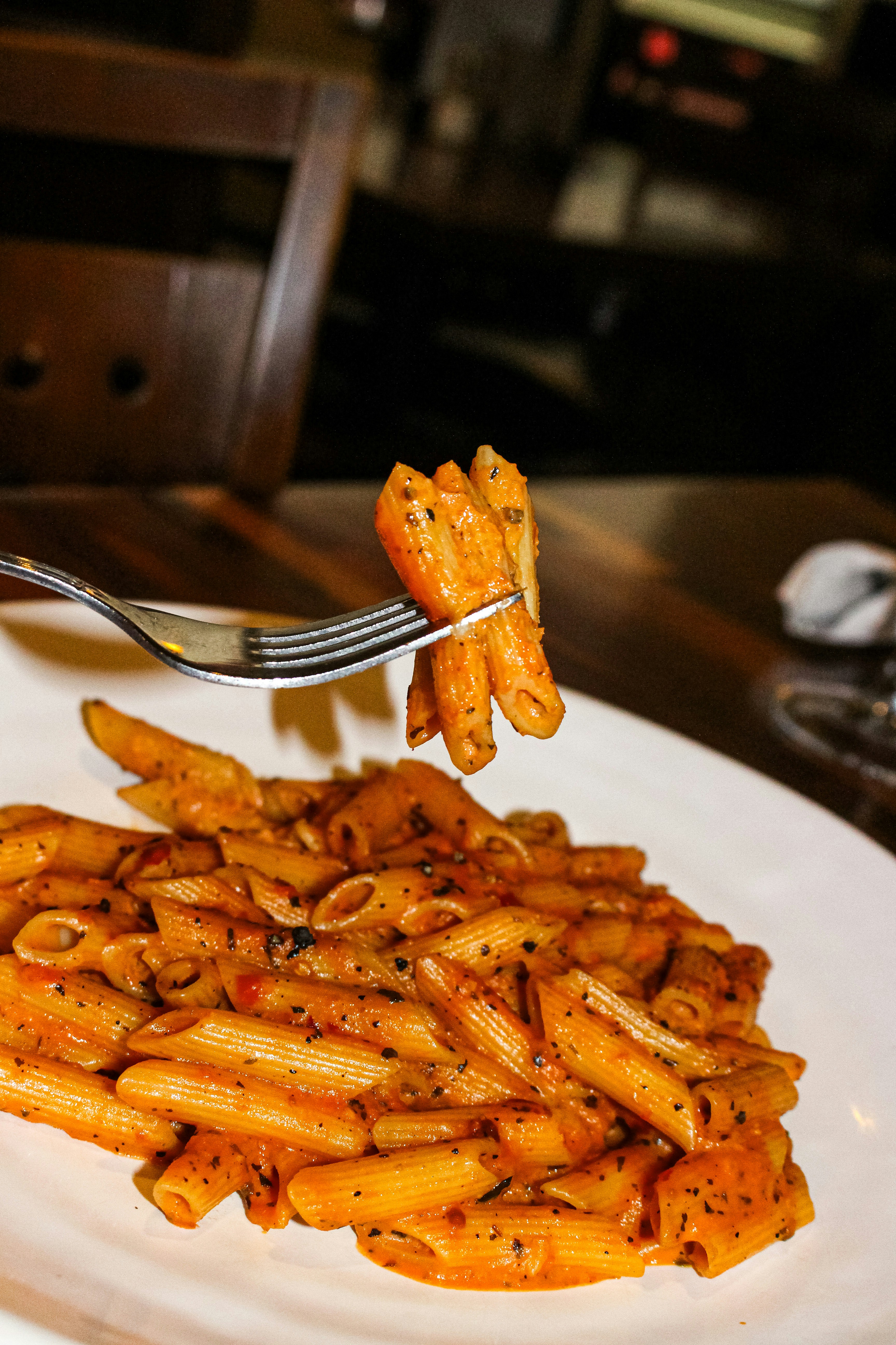 A fork lifts penne pasta coated in red sauce.