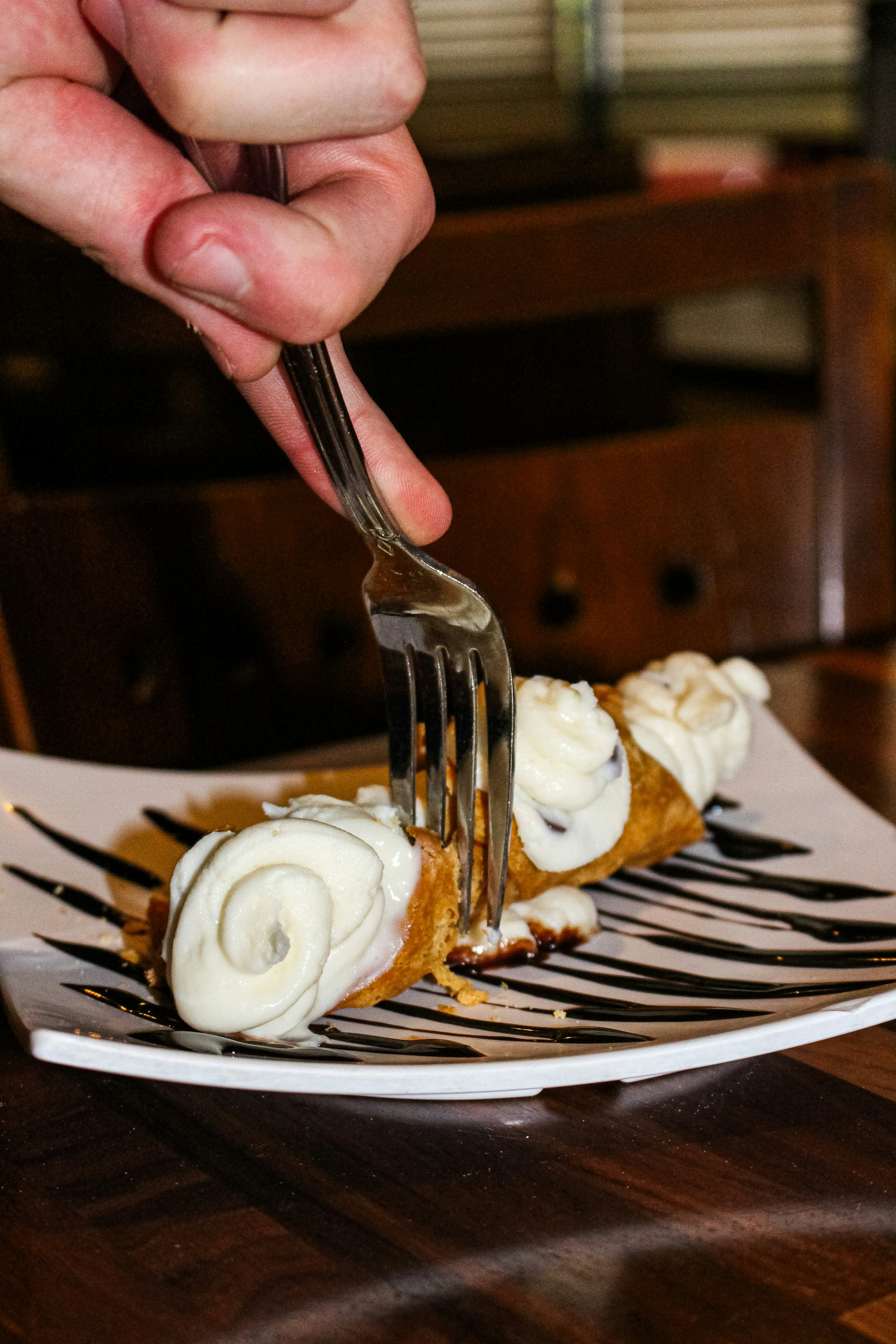 A hand uses a fork to eat a cannoli