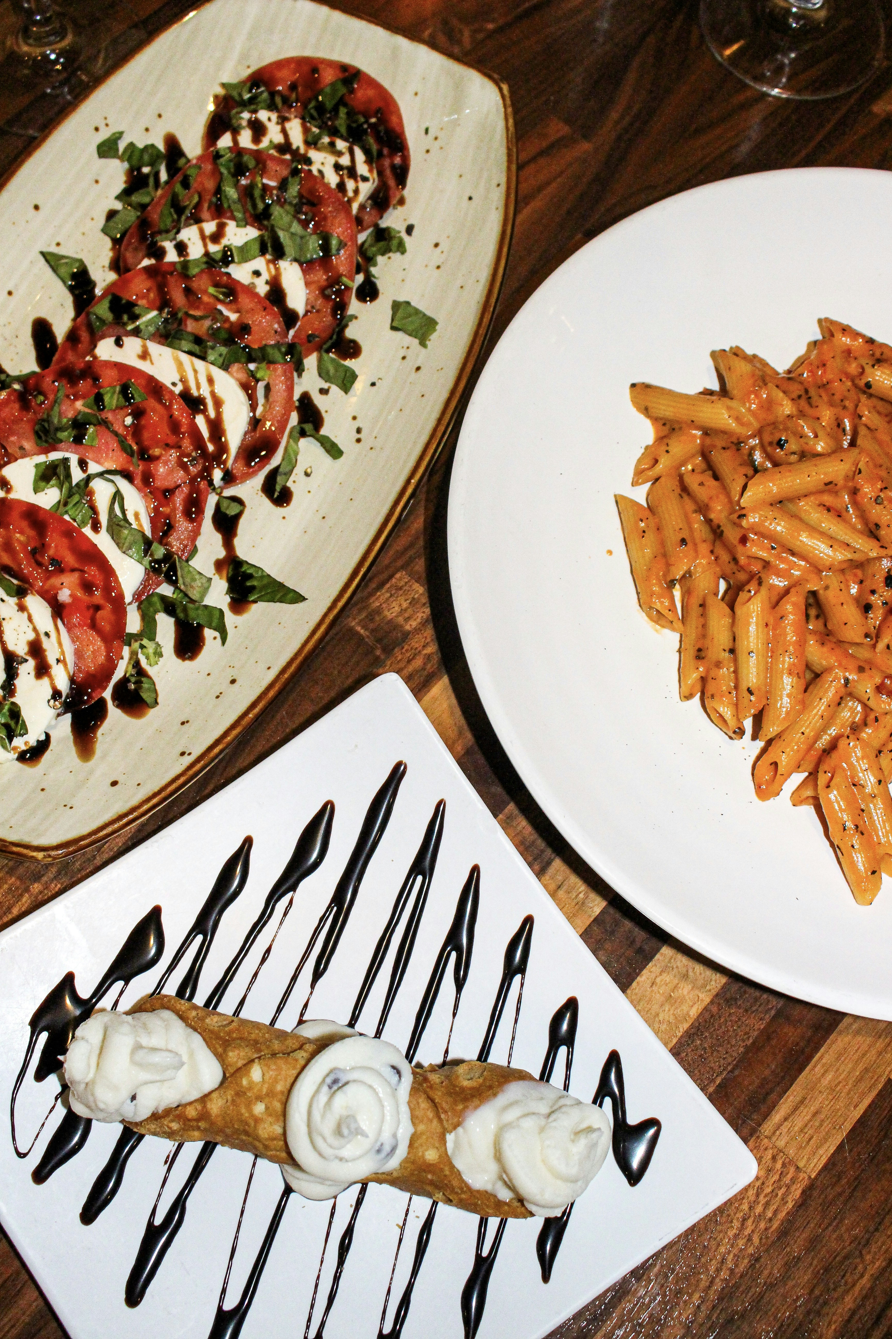 Caprese salad, penne pasta, and cannoli on table