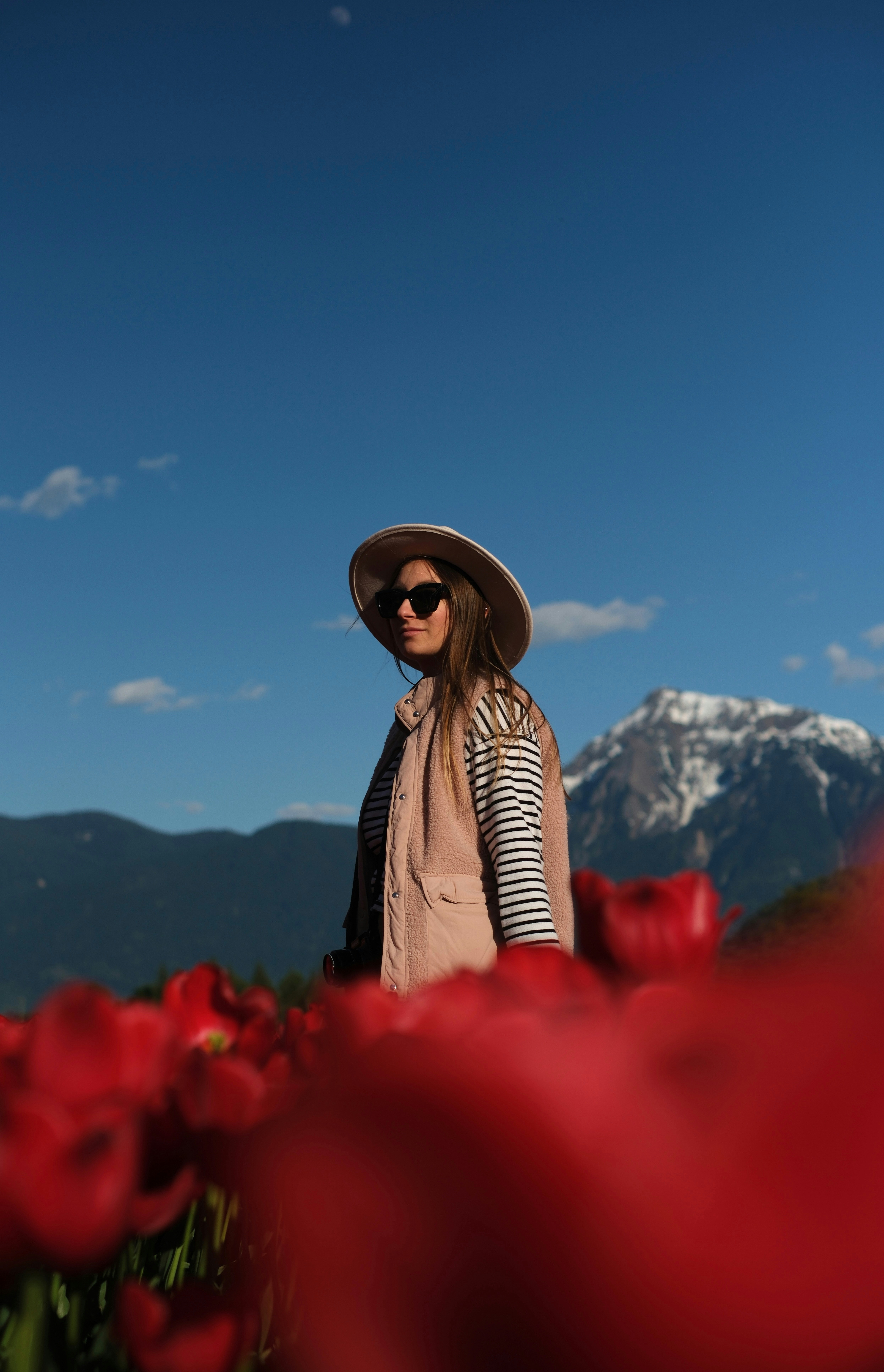 Woman in hat and vest among red tulips with mountains