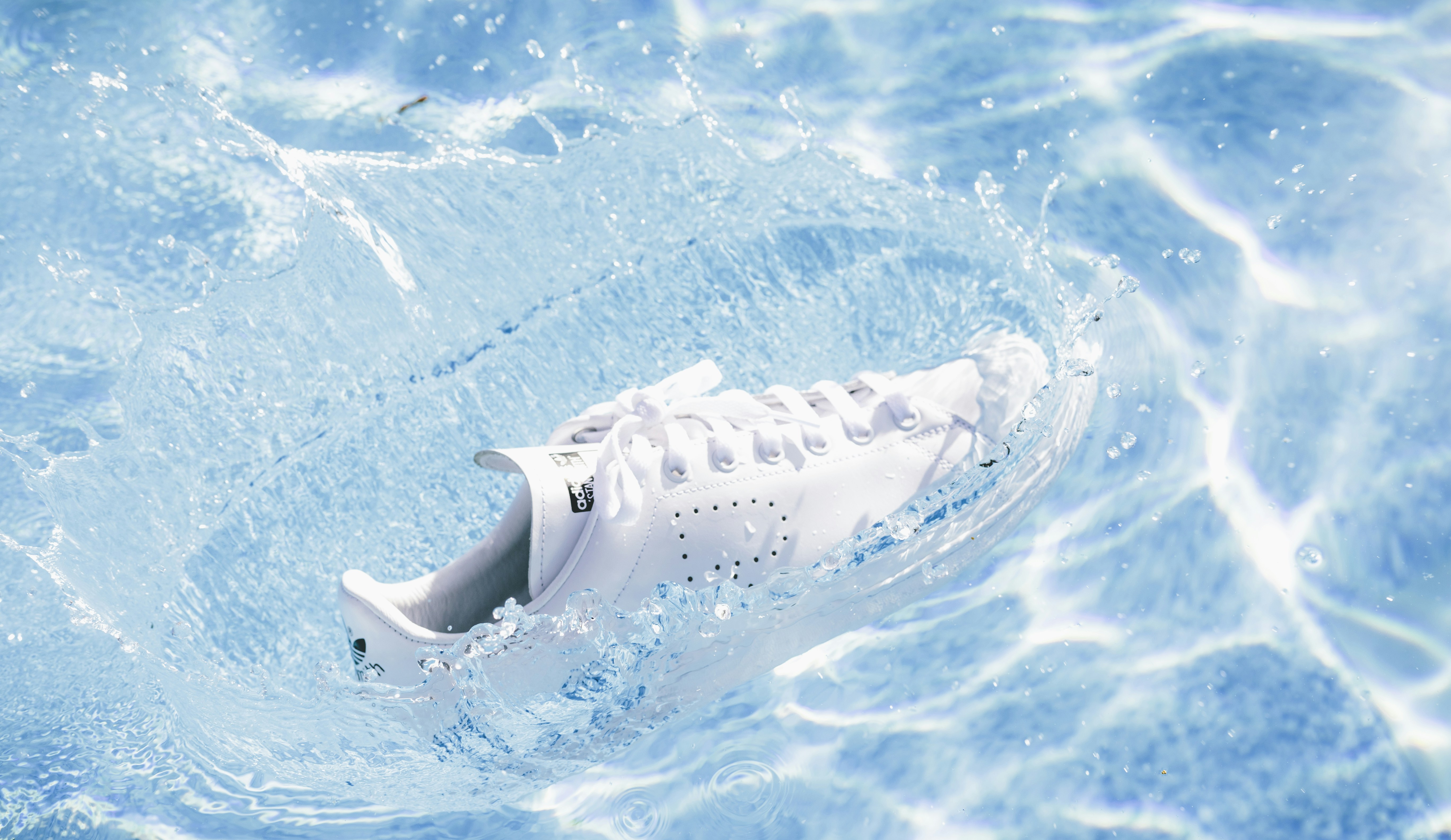 A white sneaker splashes into clear blue water.