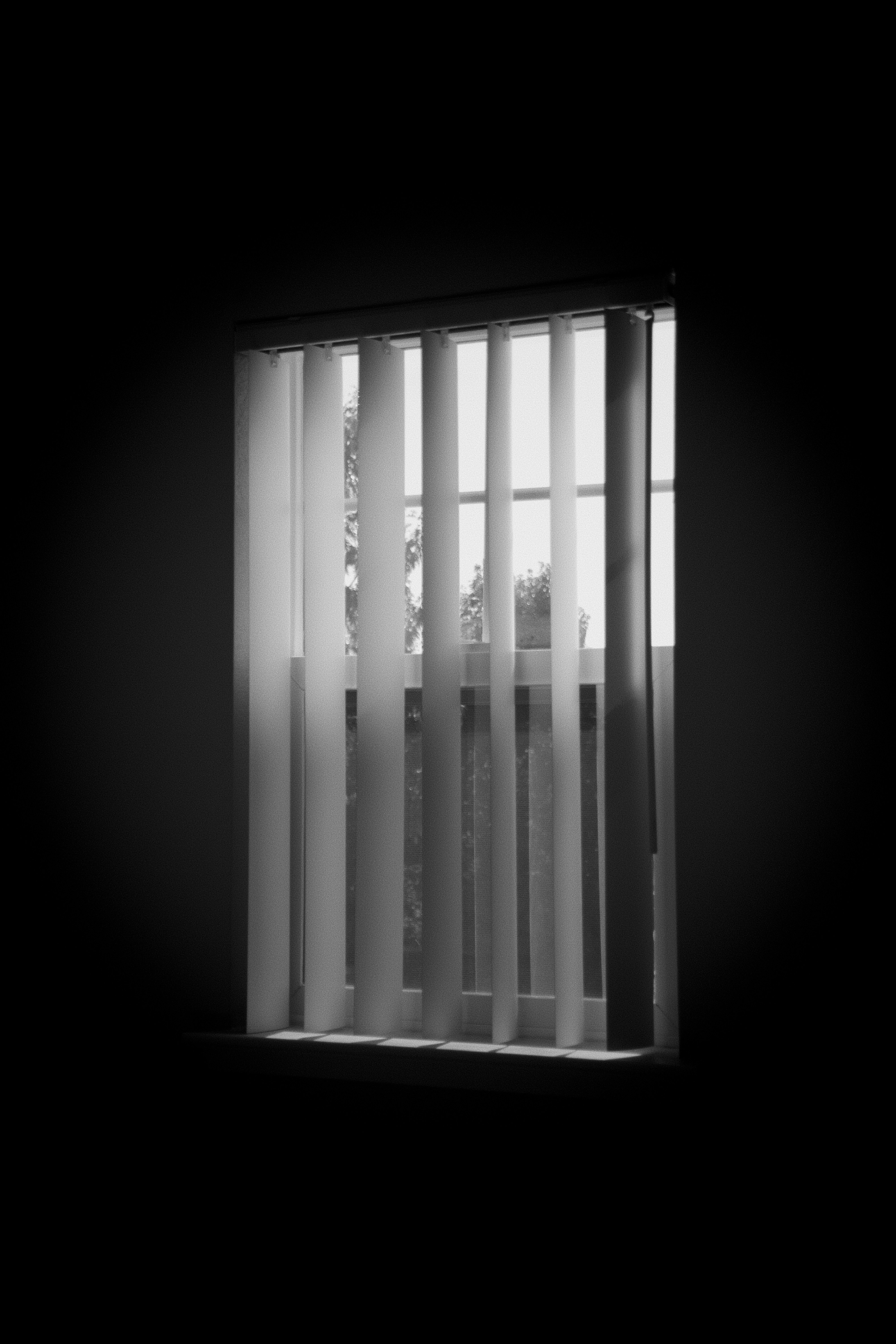Vertical blinds partially covering a window with light filtering through.