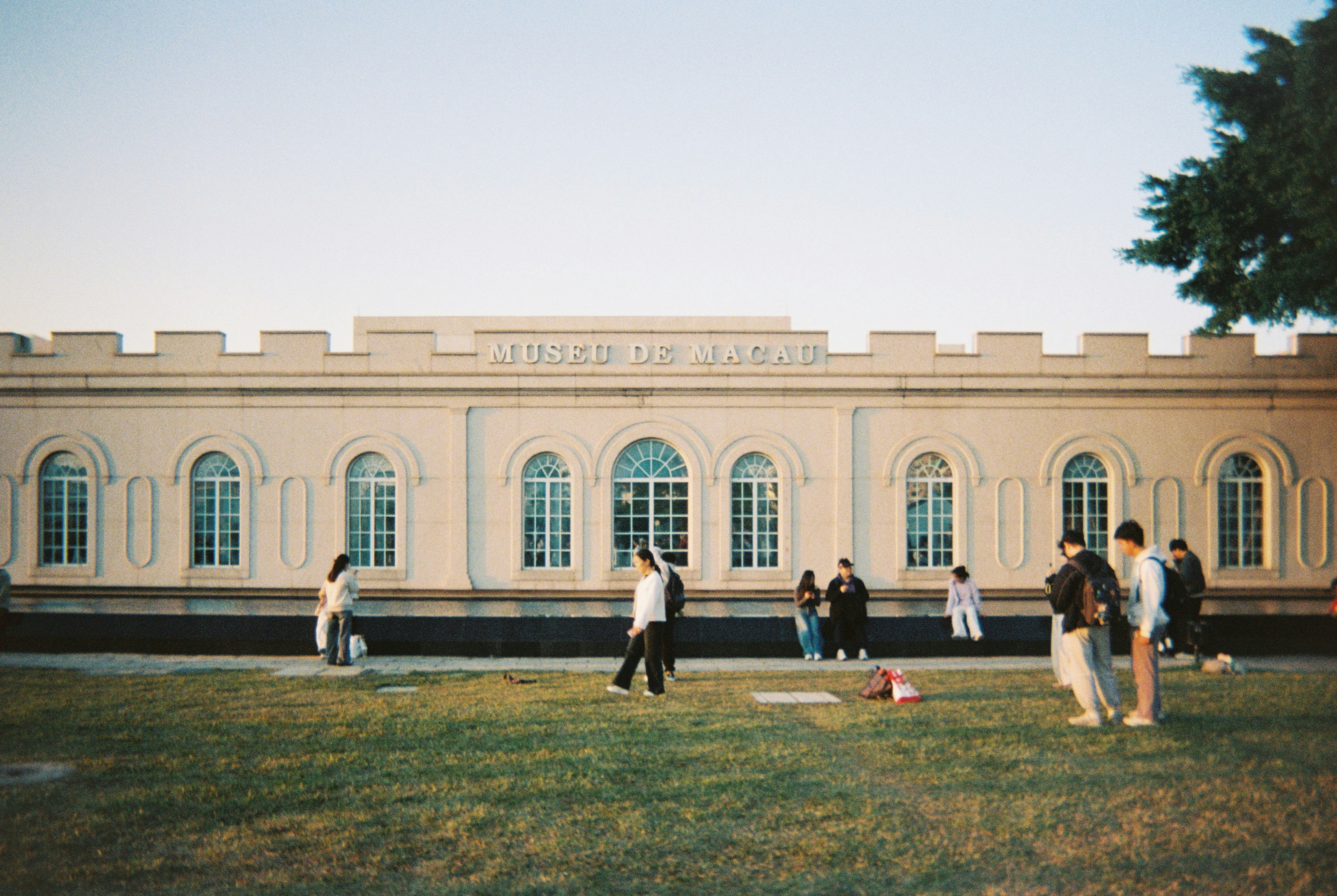 People gather in front of a long, light-colored building.