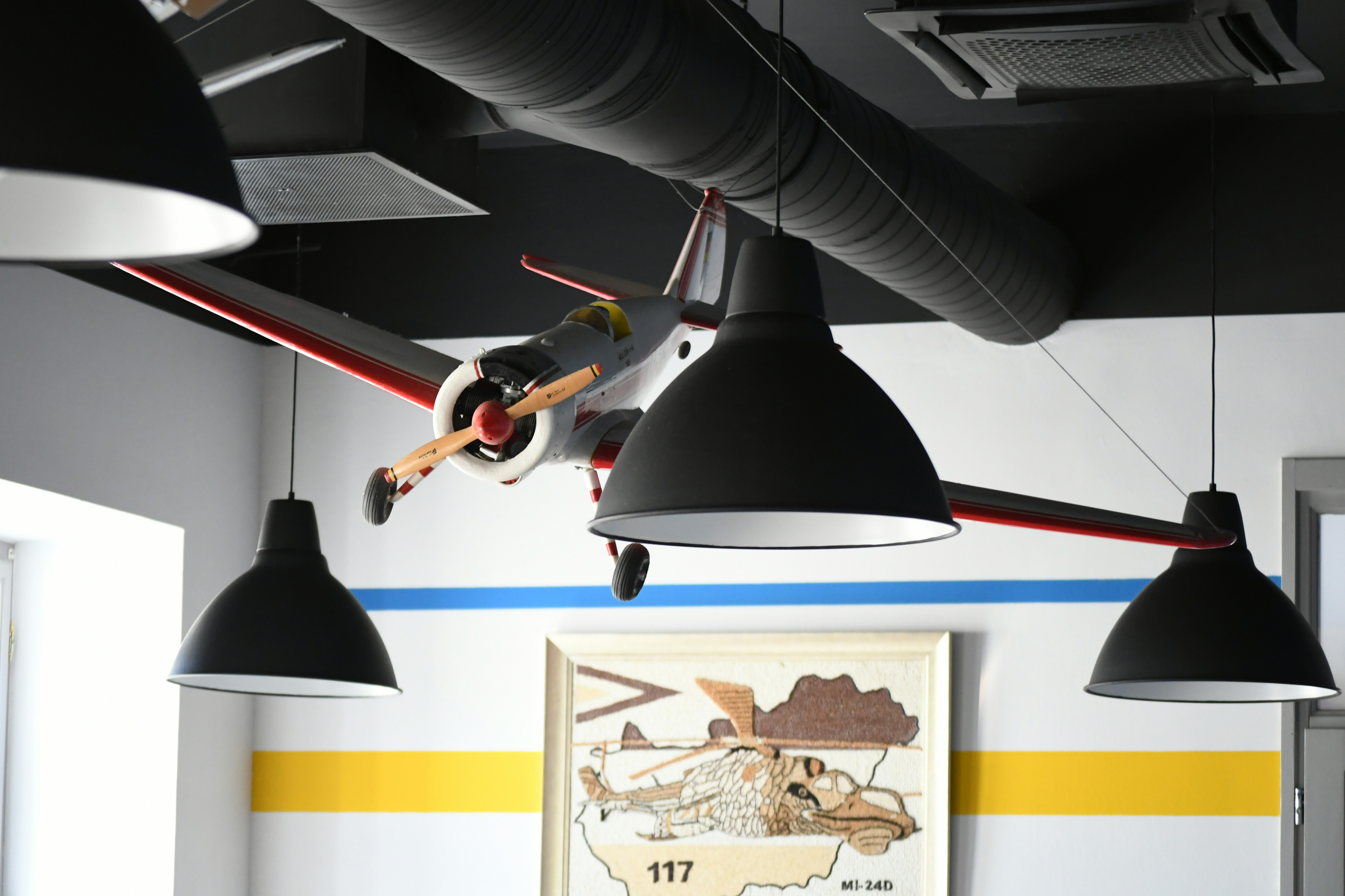 Model airplane hanging from ceiling with industrial lamps.