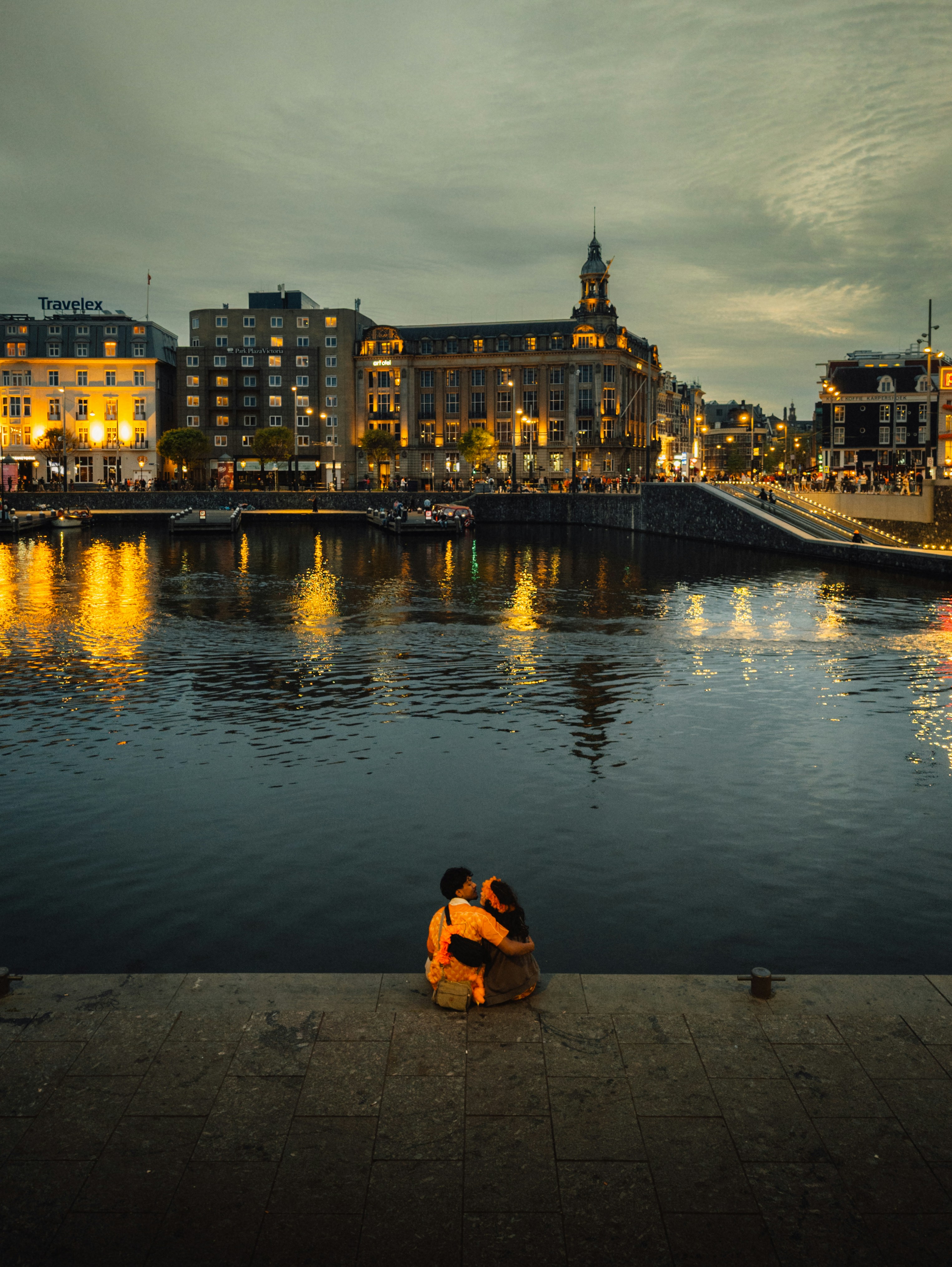 Couple embracing by canal in illuminated city at dusk