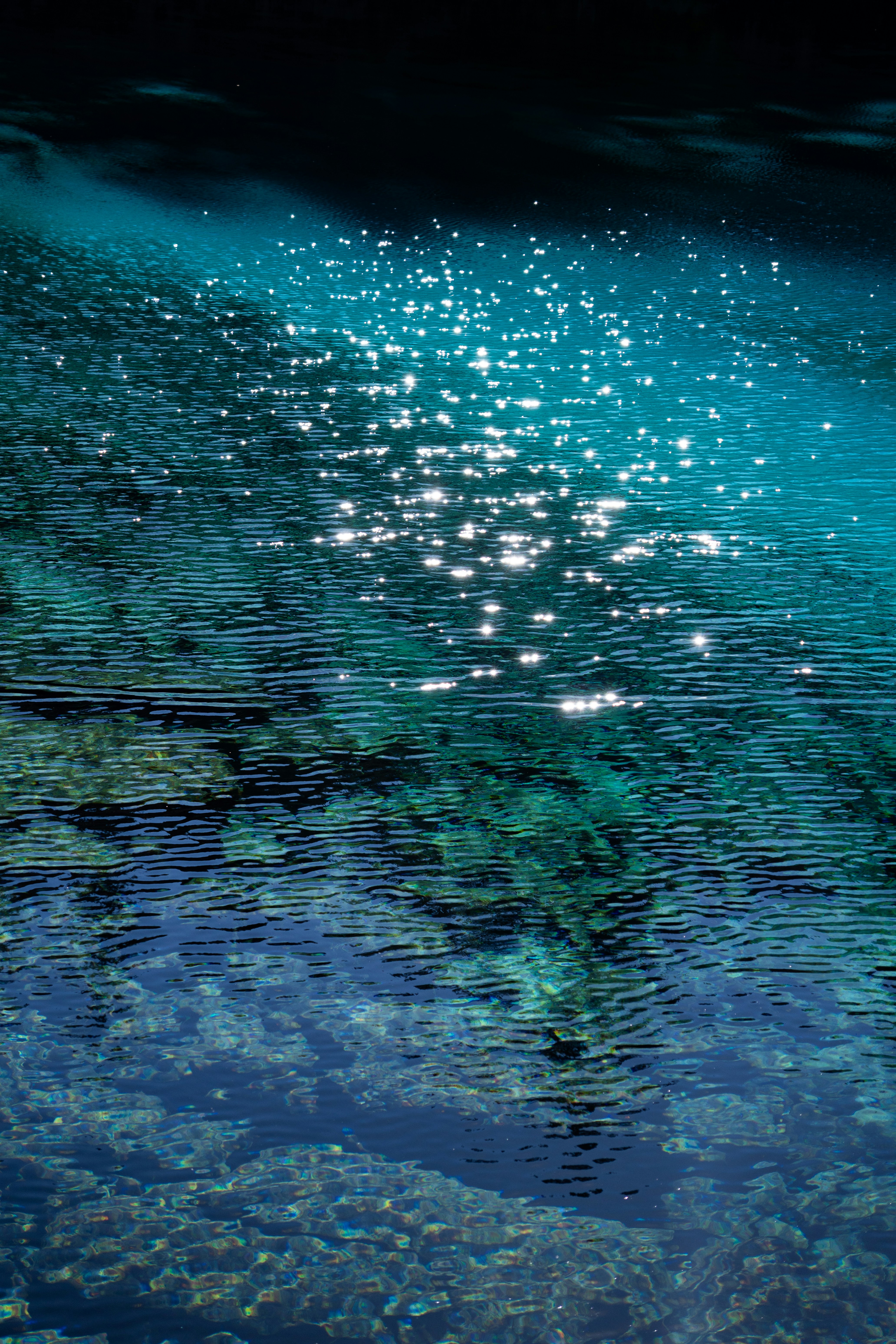 Sparkling sunlight on clear turquoise water with rocks below
