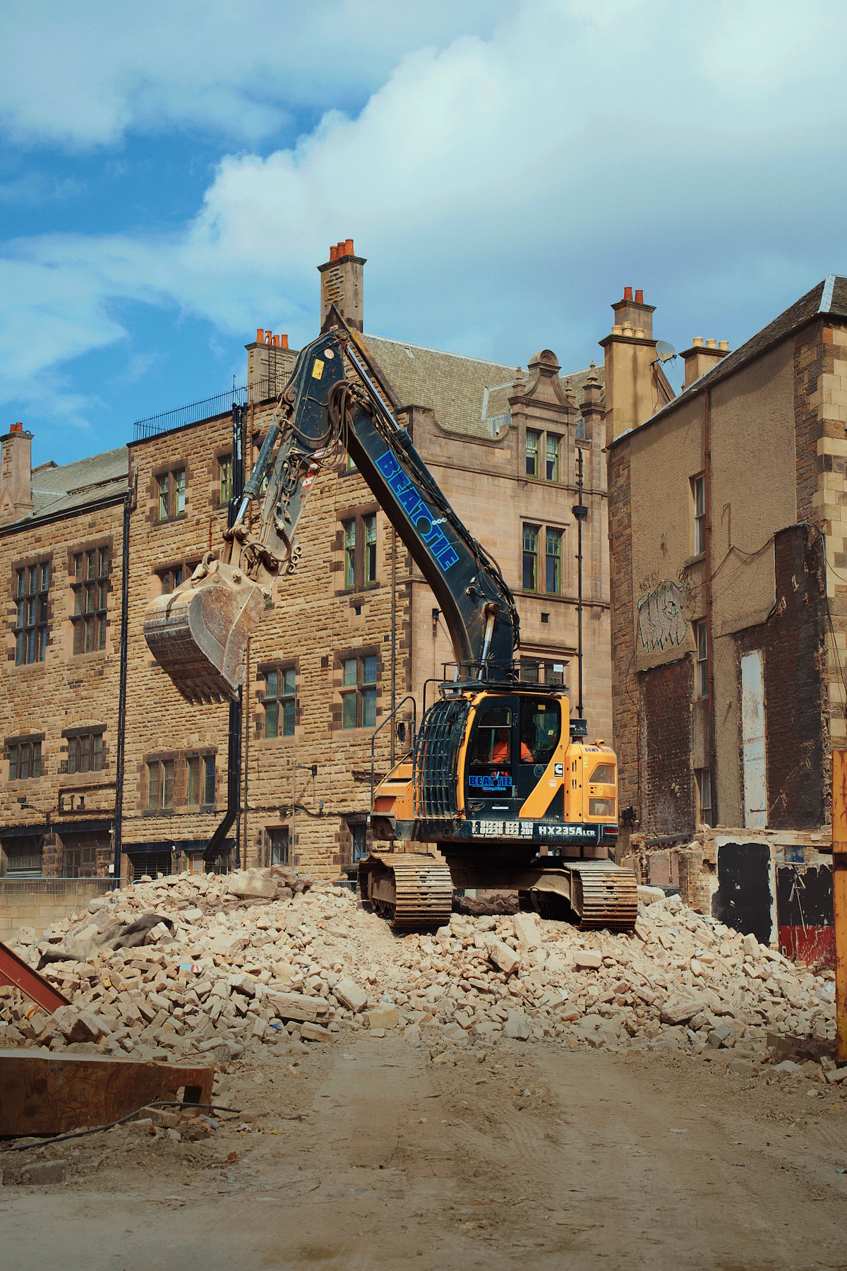 Excavator demolishing a brick building under a blue sky