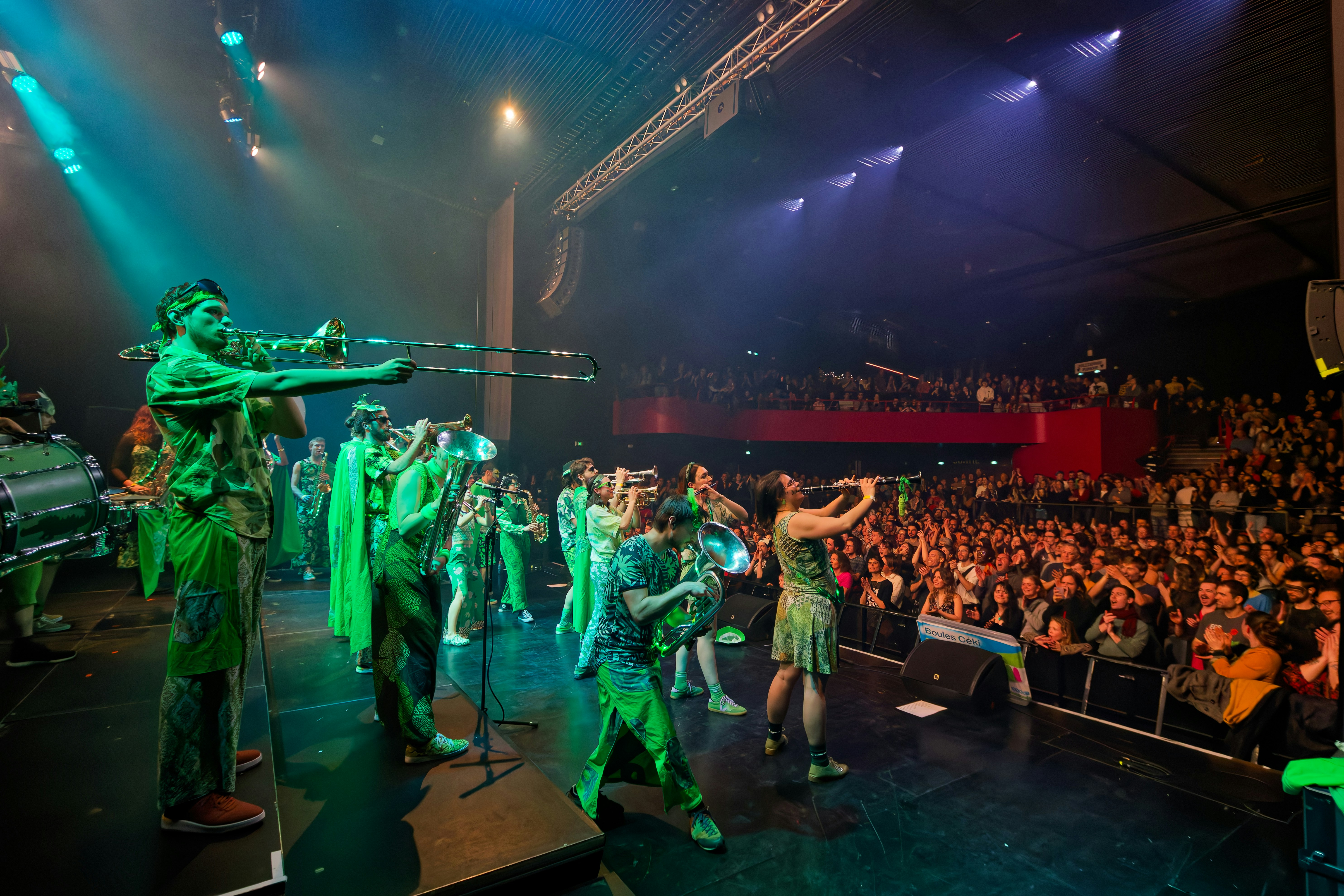 Performers in green costumes play instruments on stage for audience.