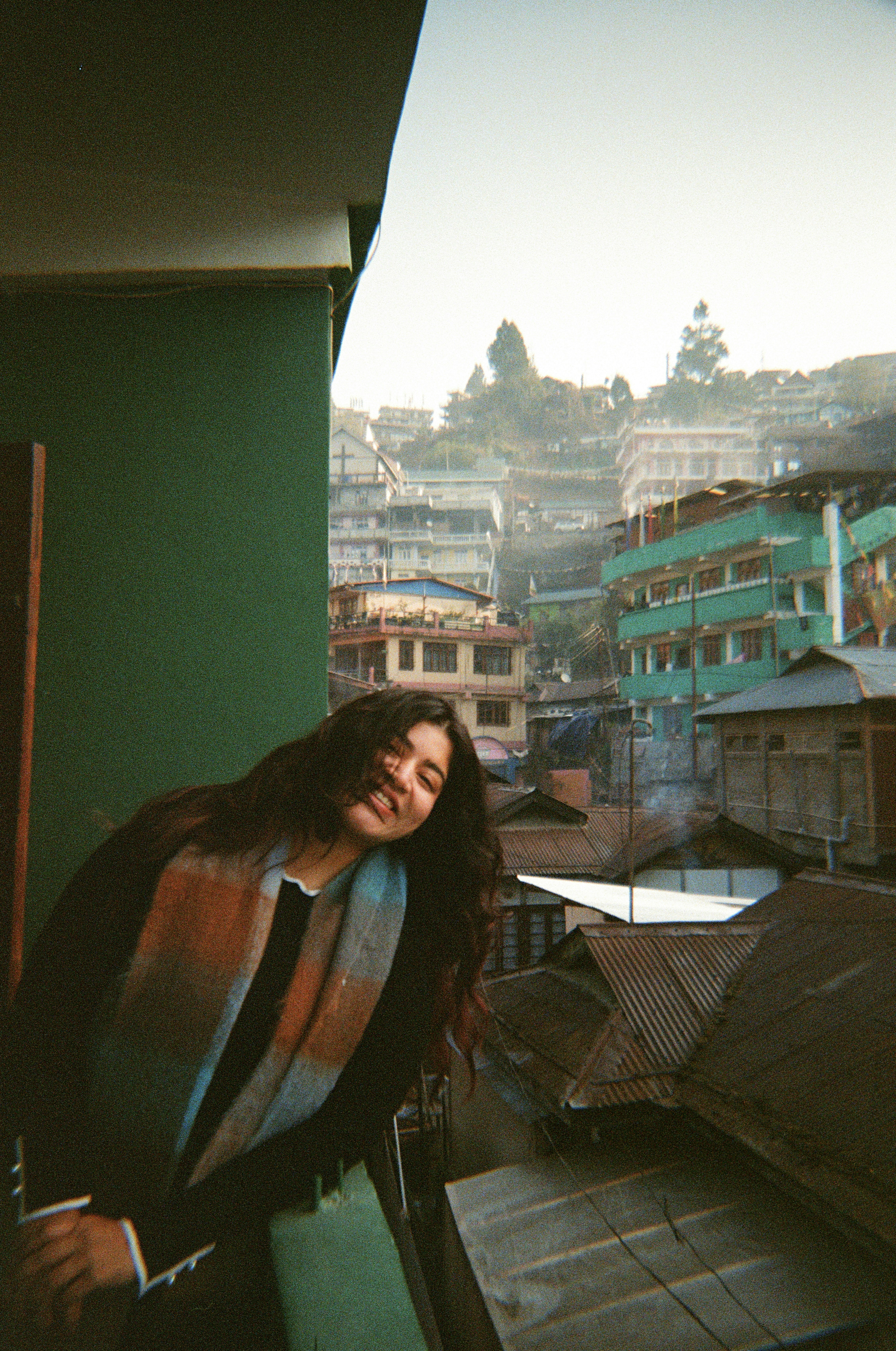 A young woman smiles on a balcony overlooking a town.