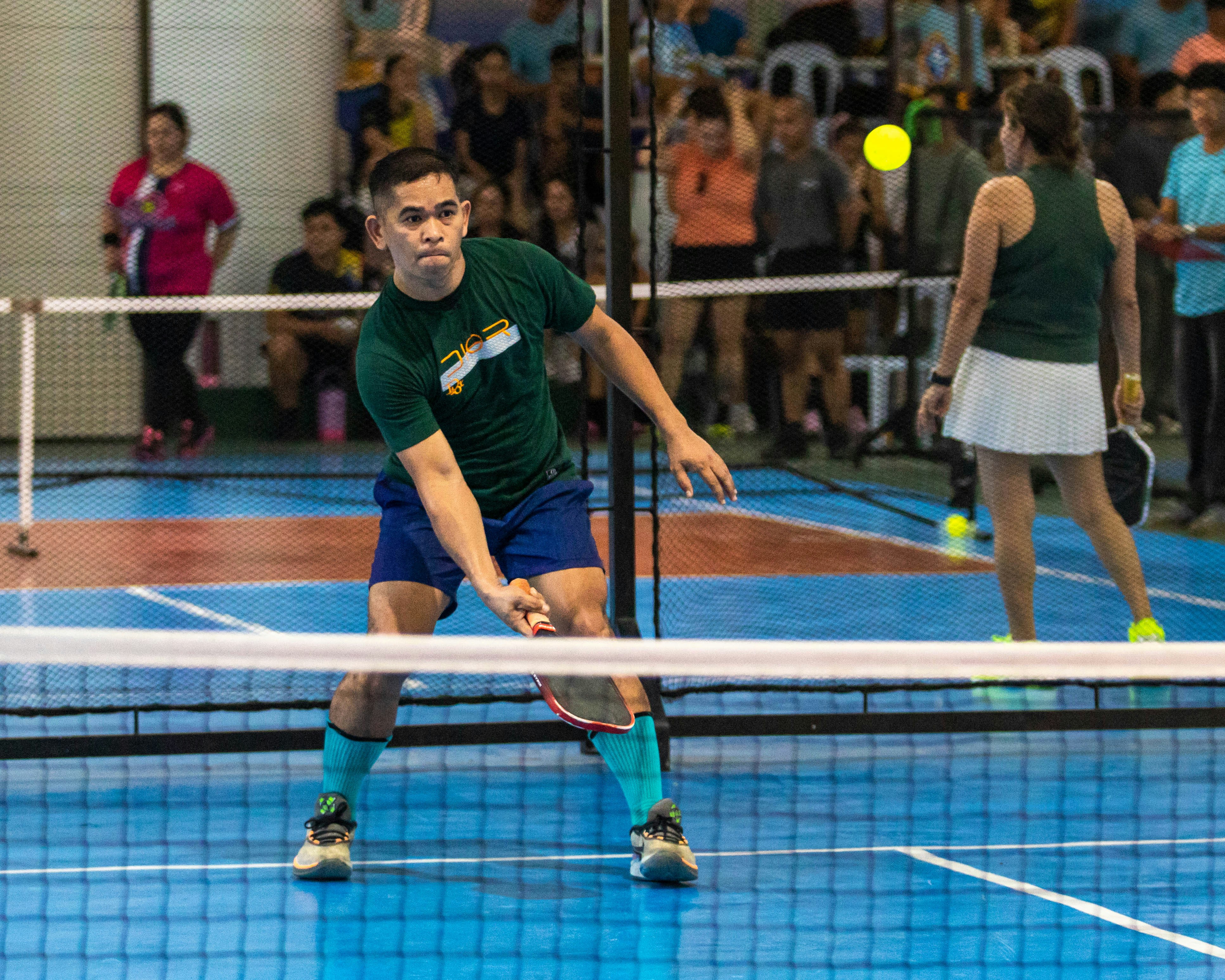A man playing pickleball with a woman in background