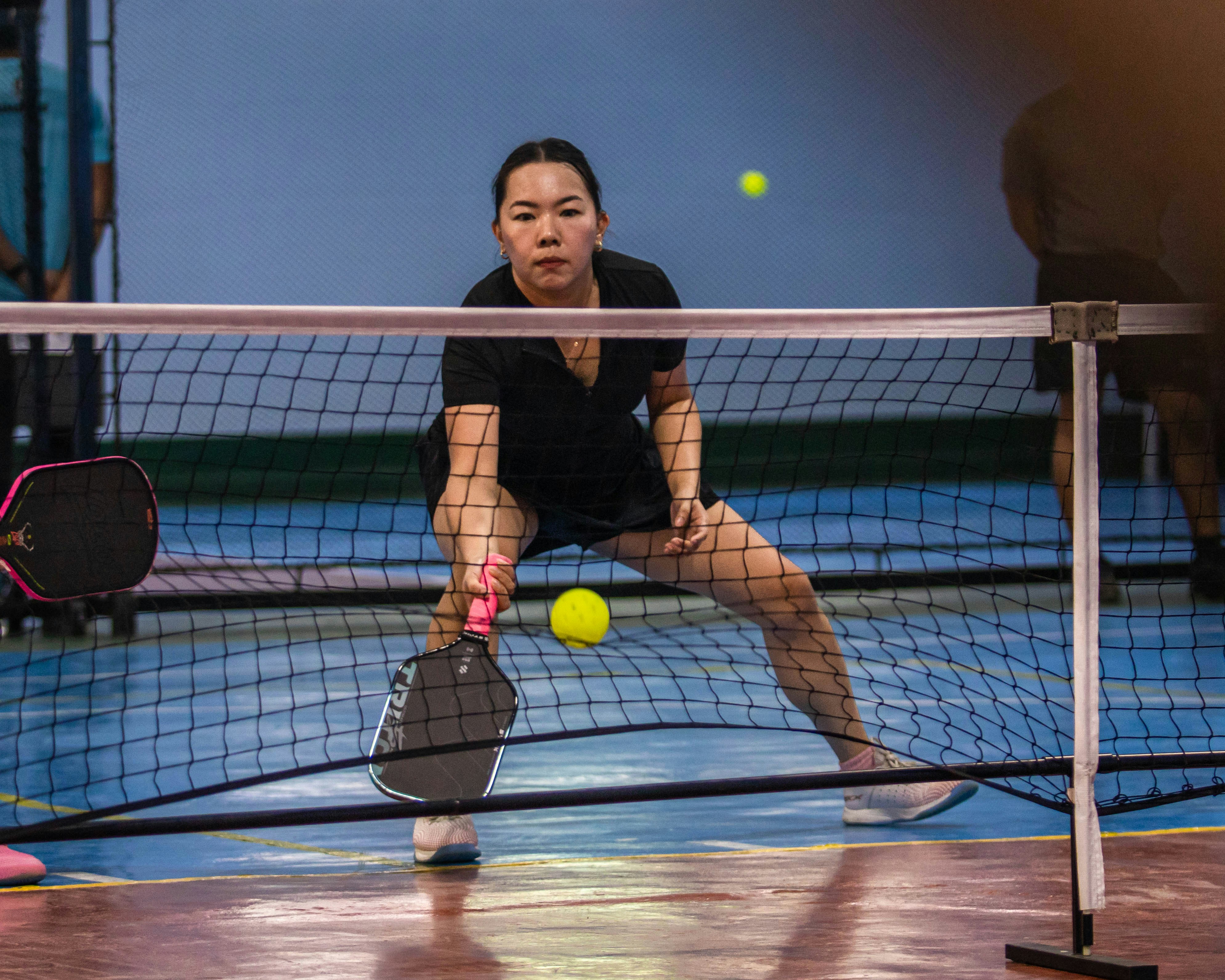 Frau spielt Pickleball, schlägt einen gelben Ball