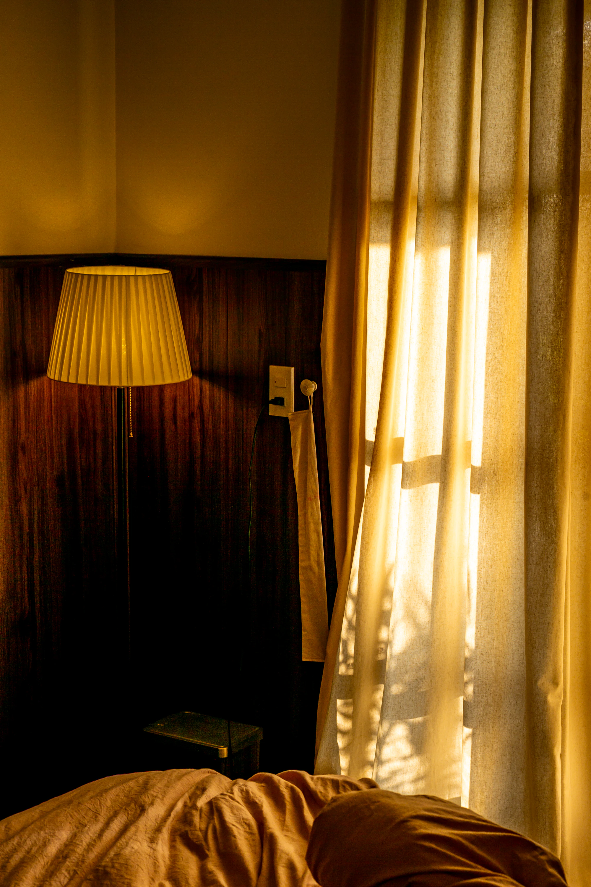 Warm lamplight and sheer curtains beside a bed