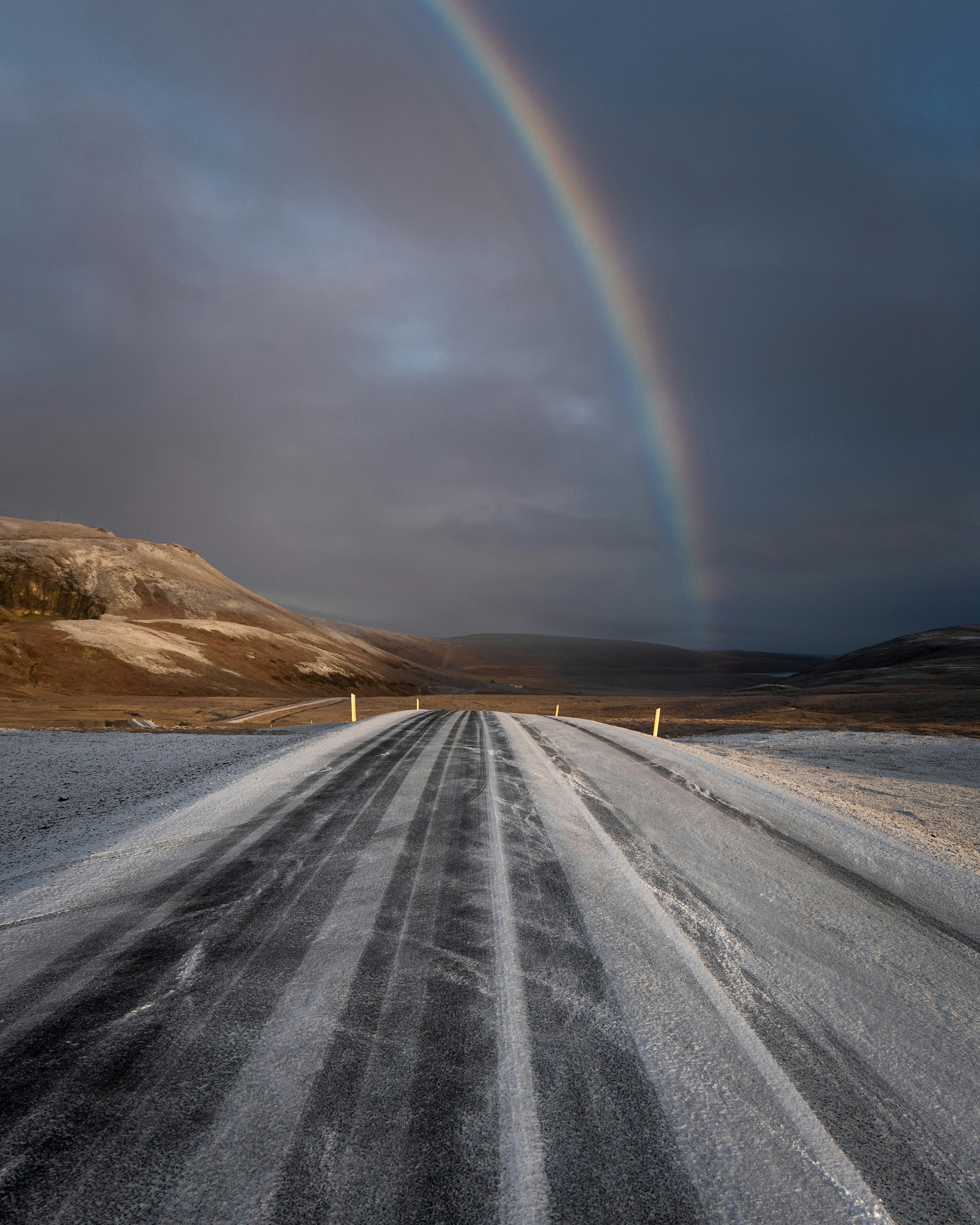 A rainbow arches over a road in a snowy landscape.