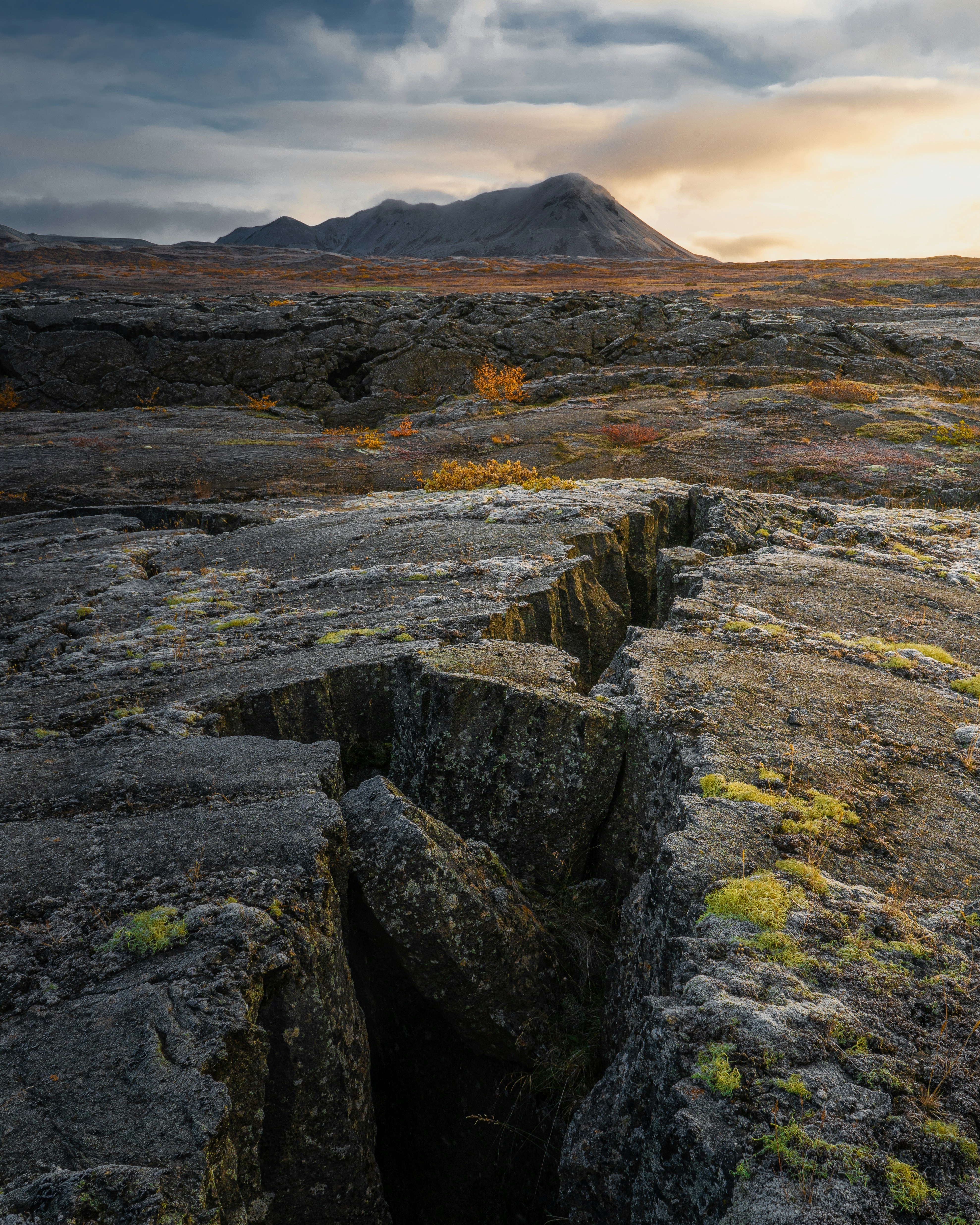Cracked volcanic rock landscape with distant mountain at sunset