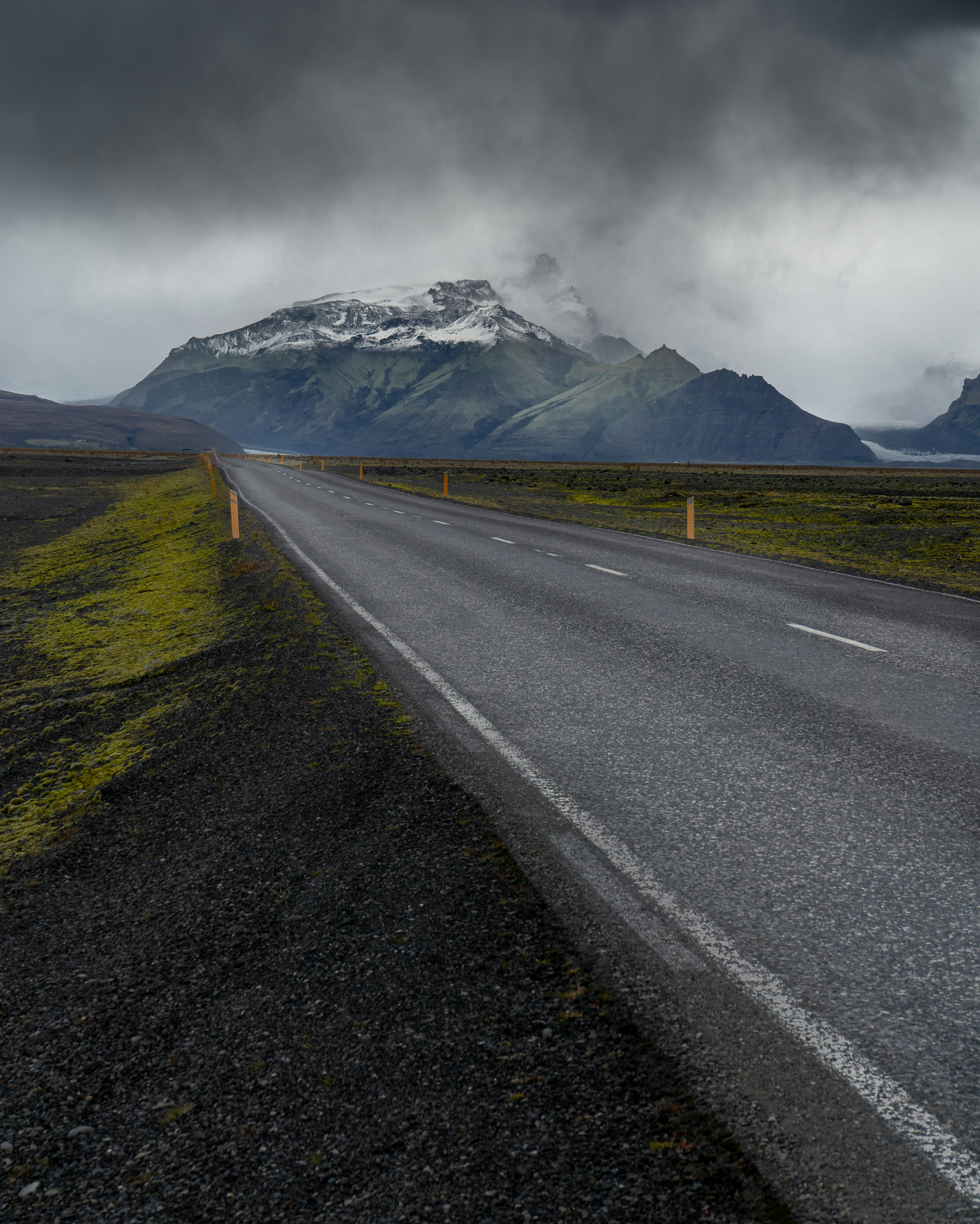 Empty road leading to snow-capped mountains under cloudy sky