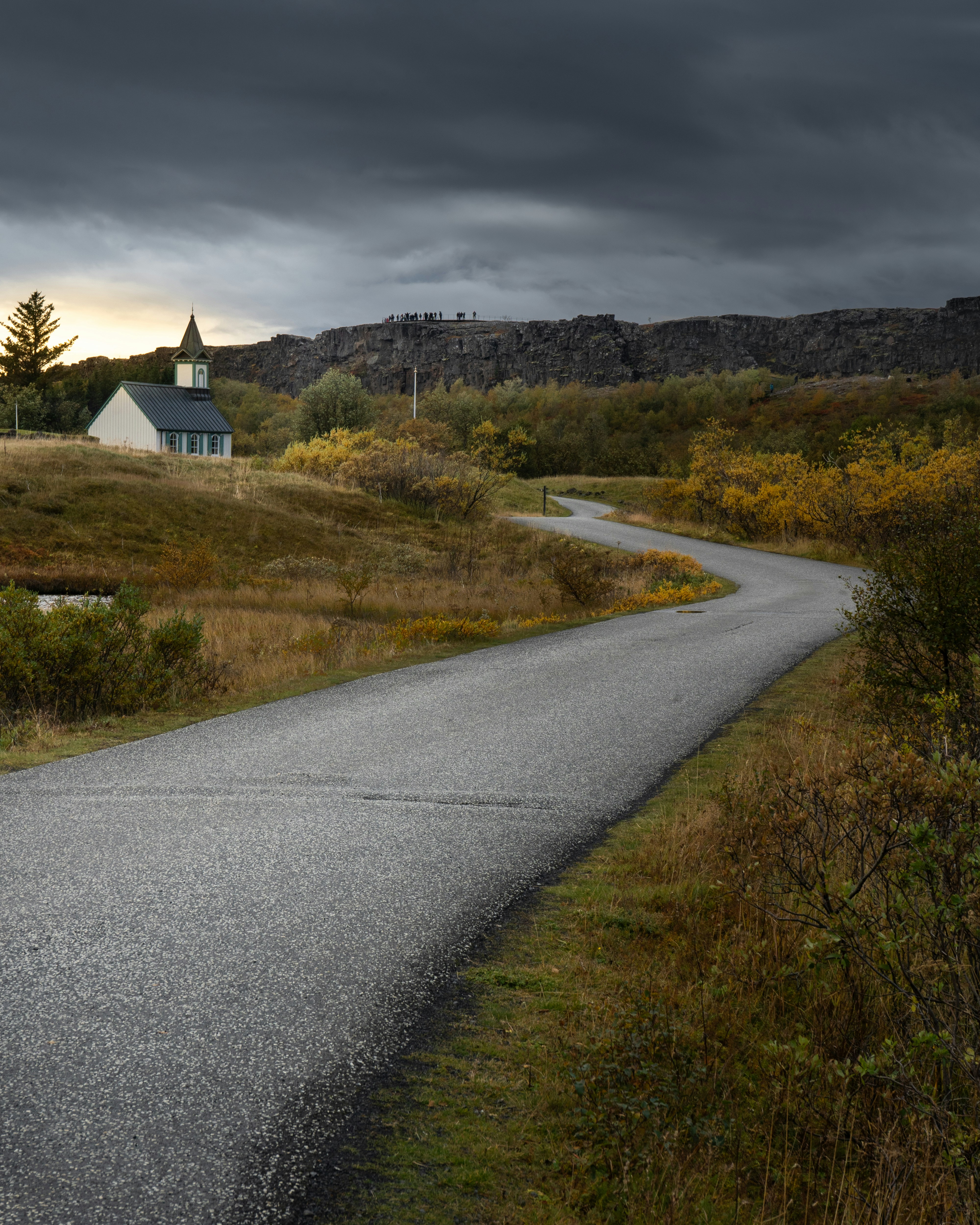 Winding road leads to a small church under stormy skies.