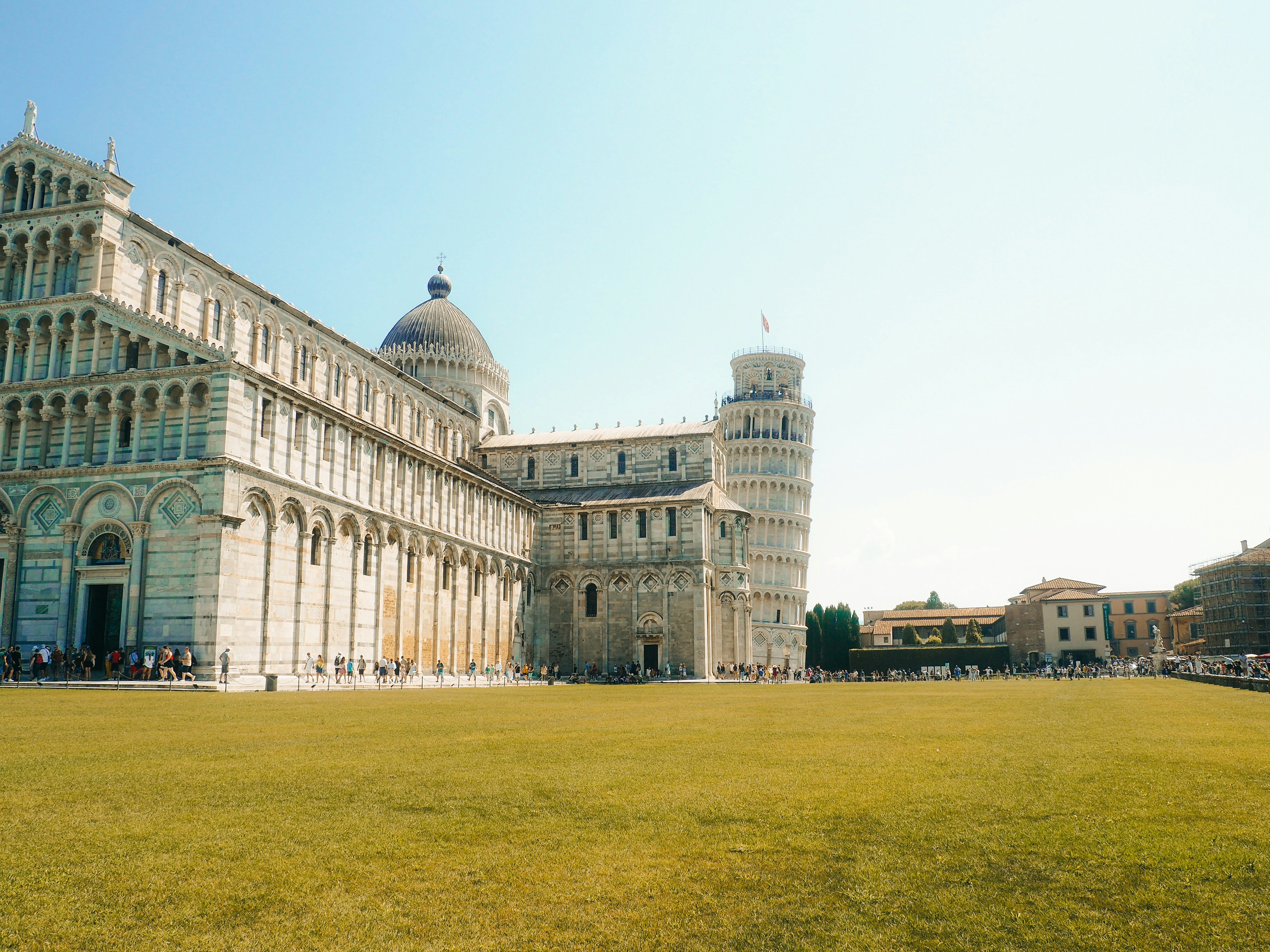 The leaning tower of pisa with a large green field.