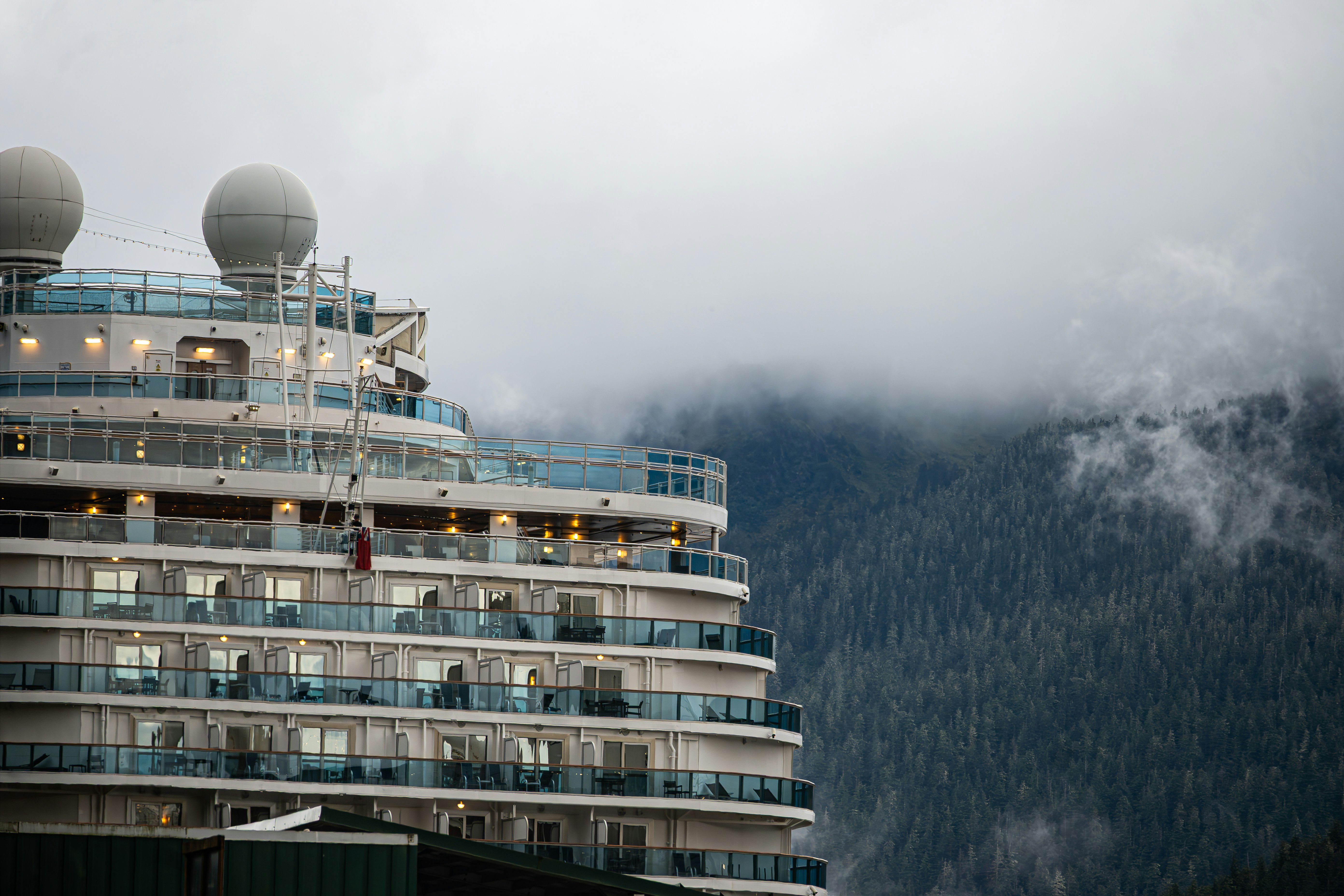 Cruise ship docked near misty, forested mountains.
