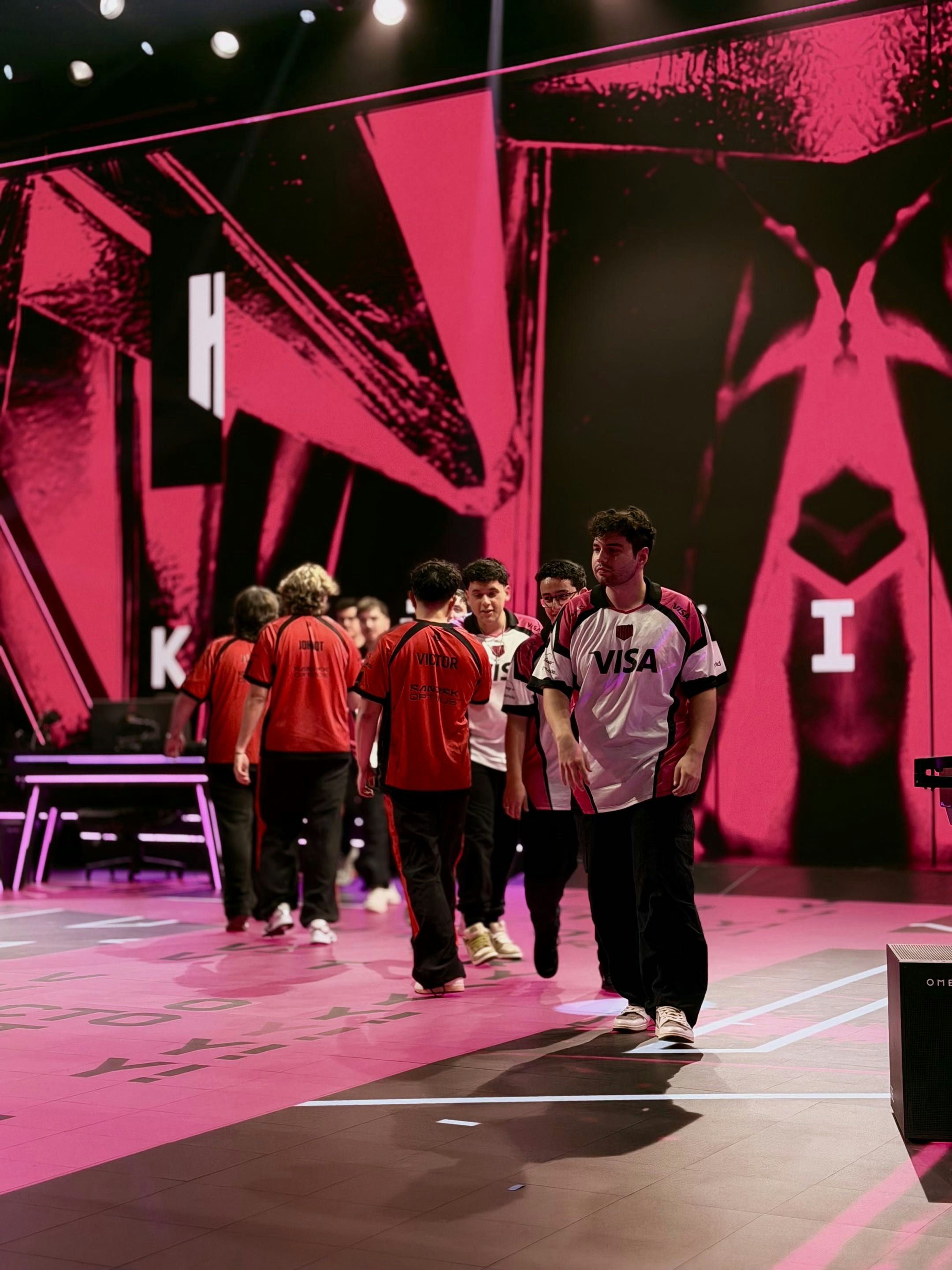 Tim esports berjalan ke atas panggung dengan latar belakang merah muda.