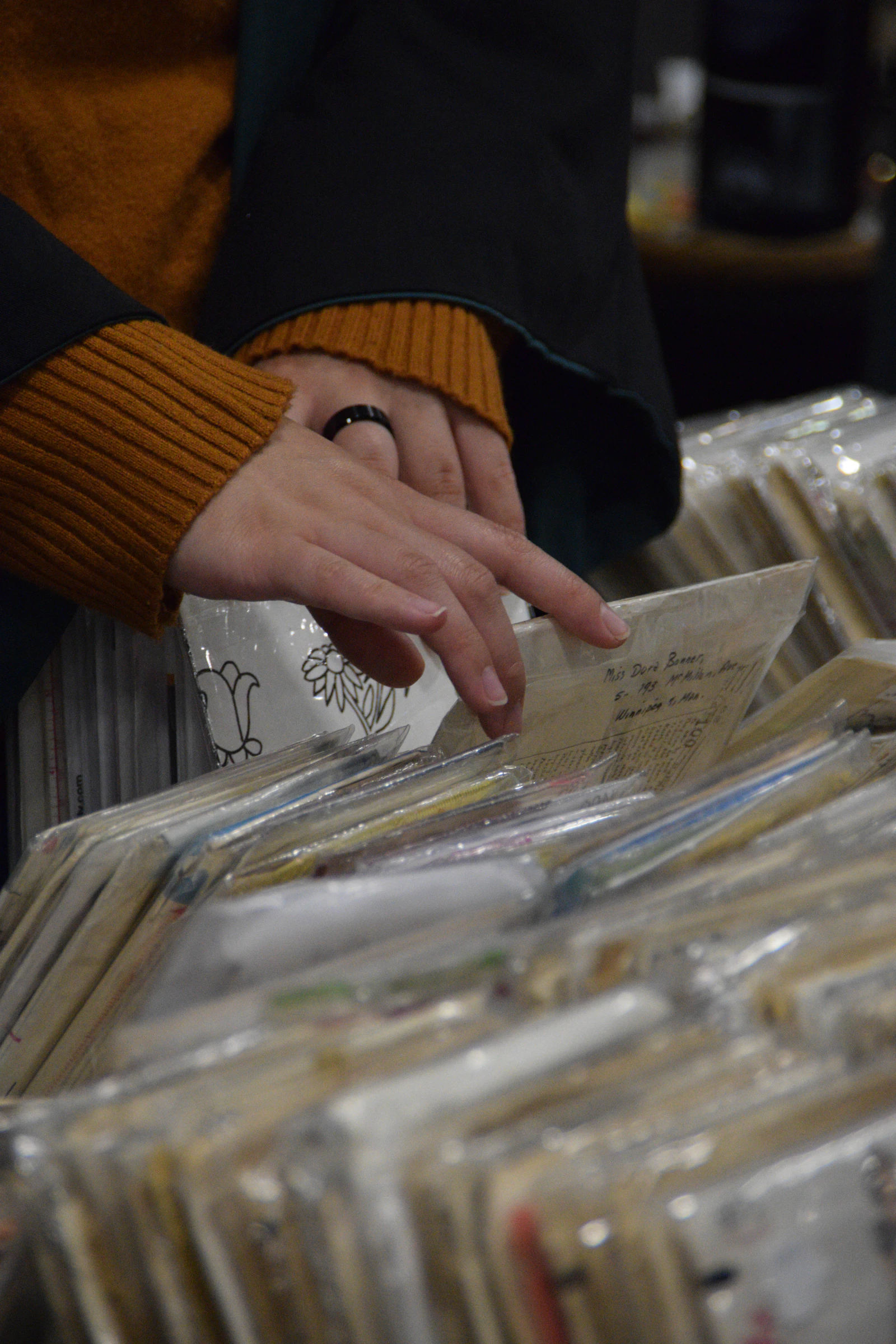 Hands in a mustard sweater flipping through a crate of record sleeves in a shop