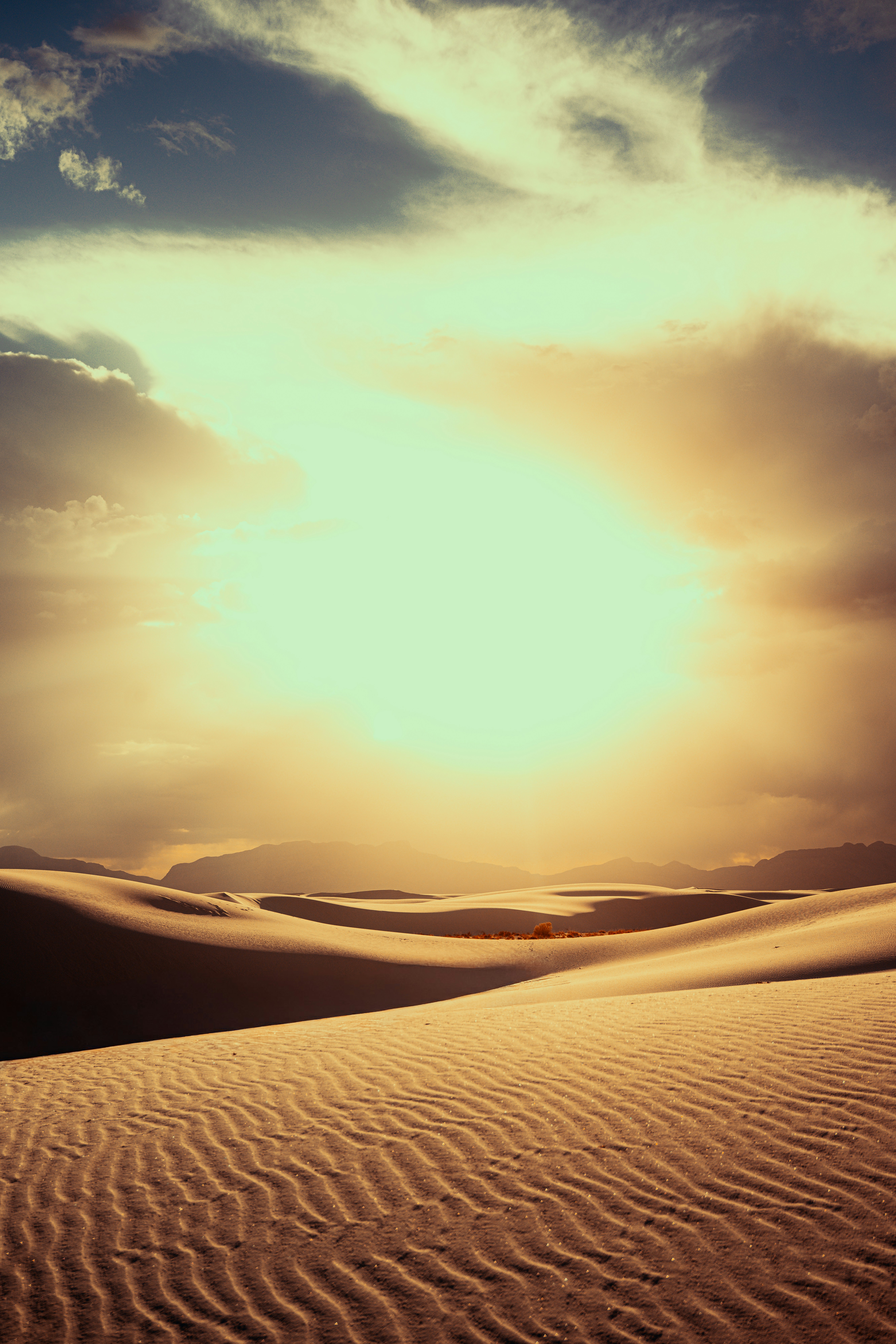 Sun shines through clouds over desert sand dunes