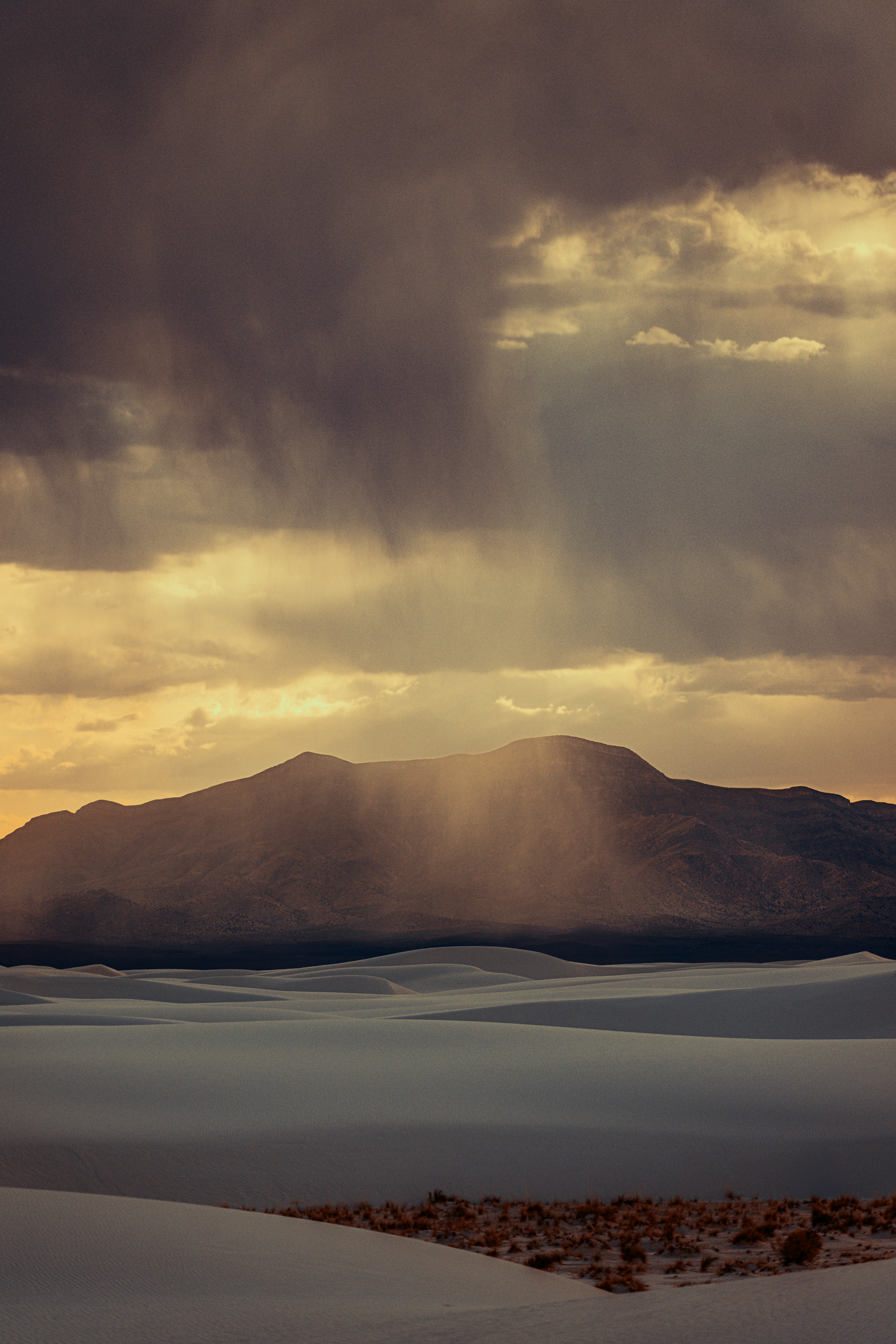 Sunbeams pierce through stormy clouds over desert dunes.