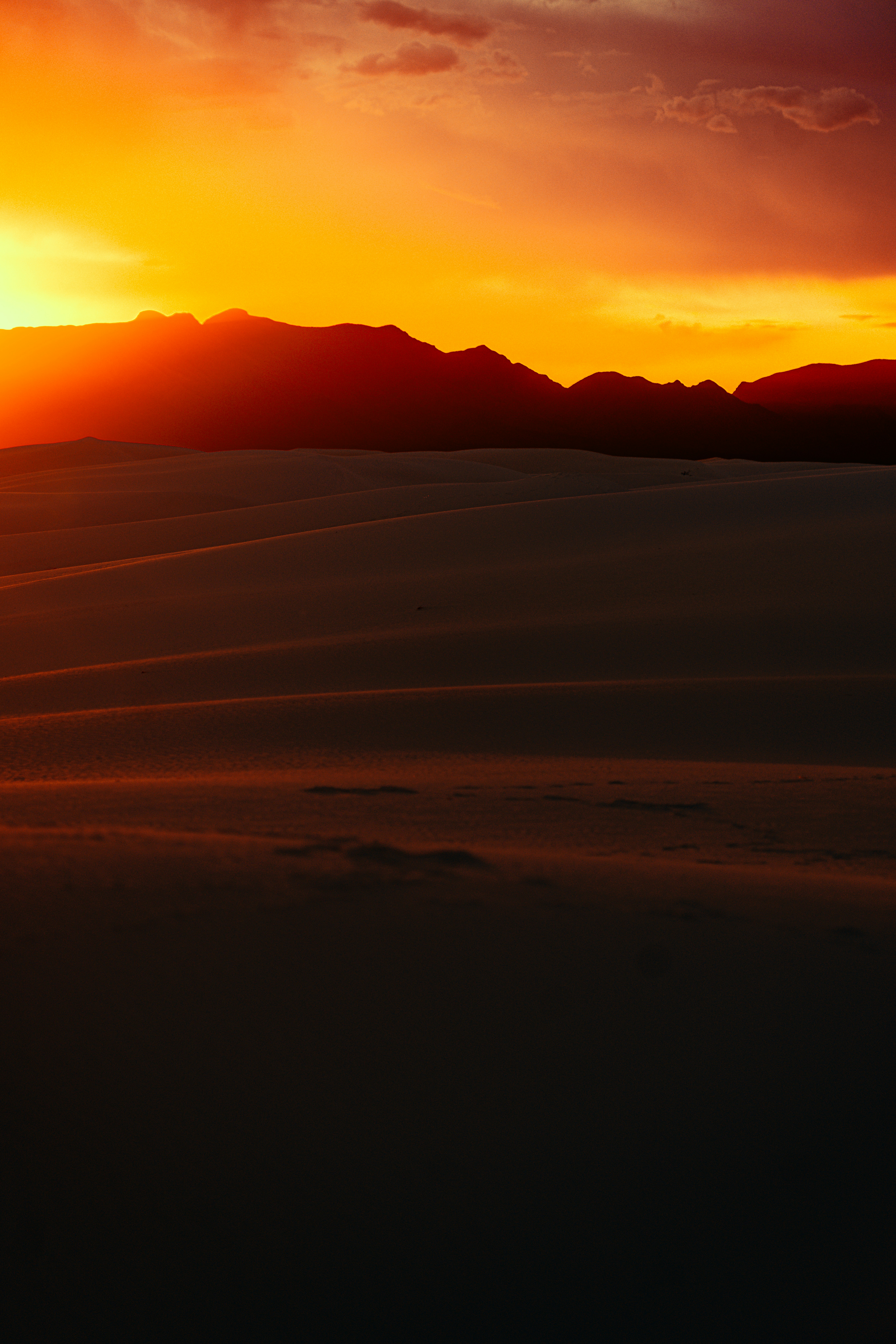 Golden sunset illuminates desert dunes and distant mountains.