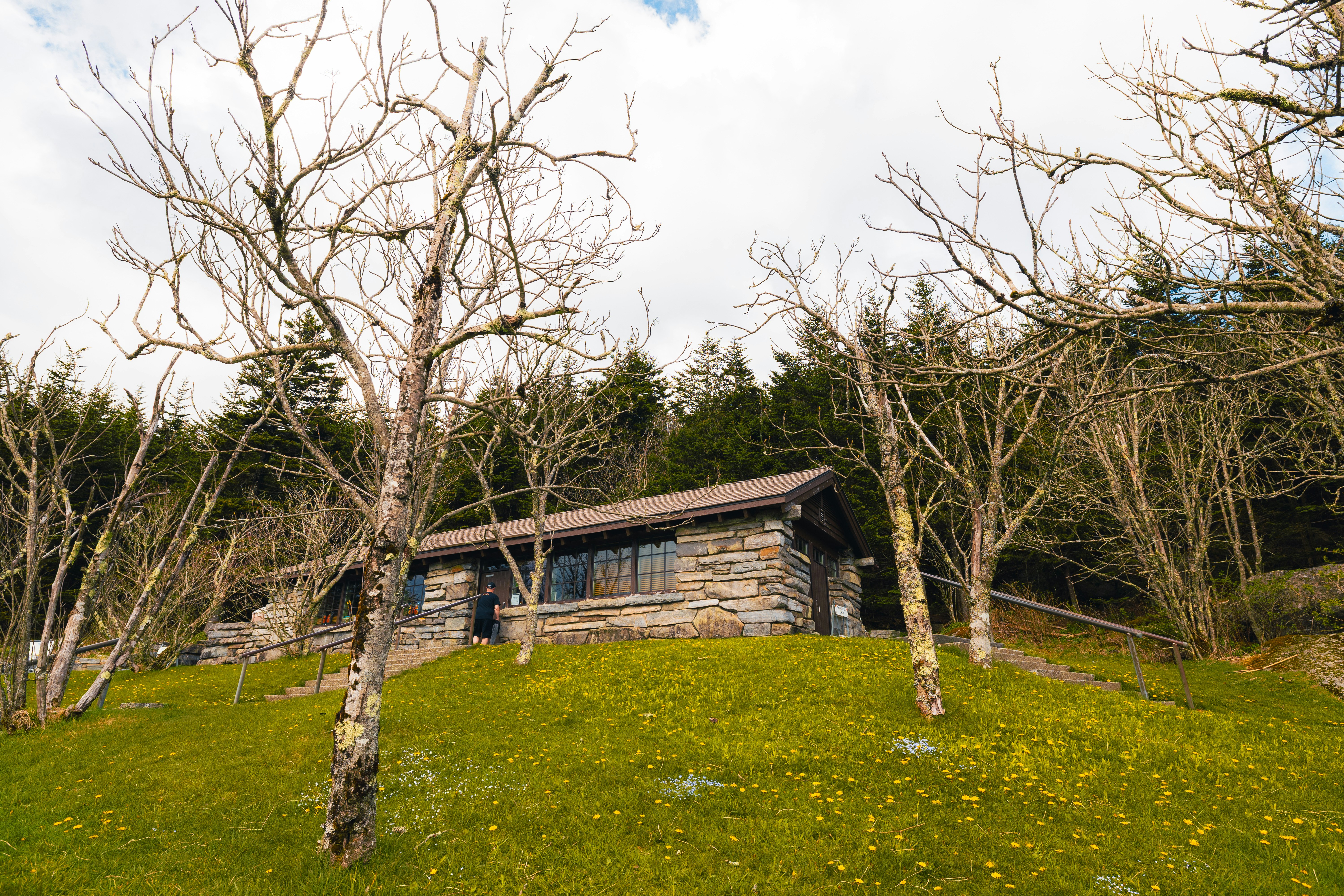 Stone cabin nestled in a grassy, wooded hillside.