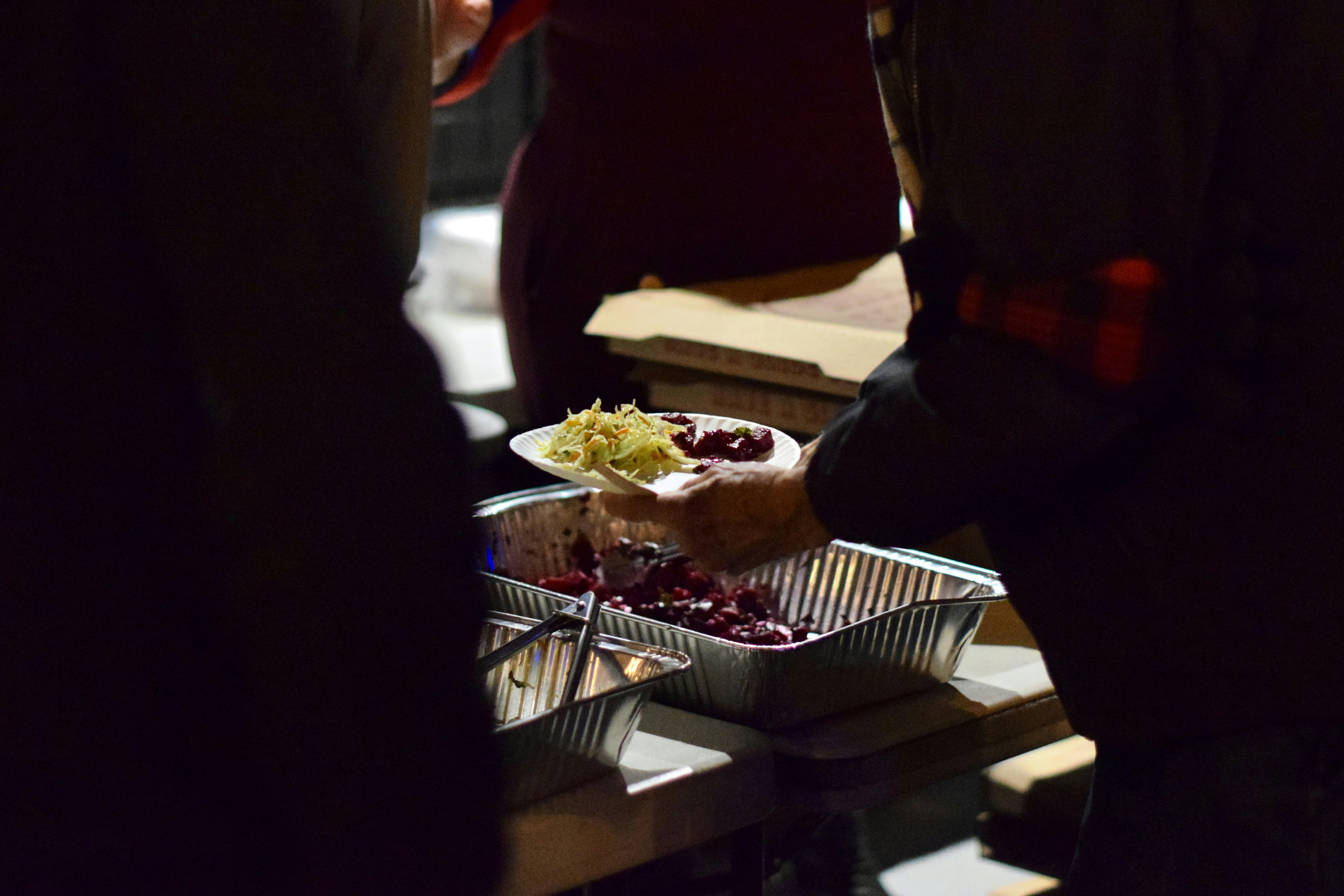 People serving food from a foil tray.