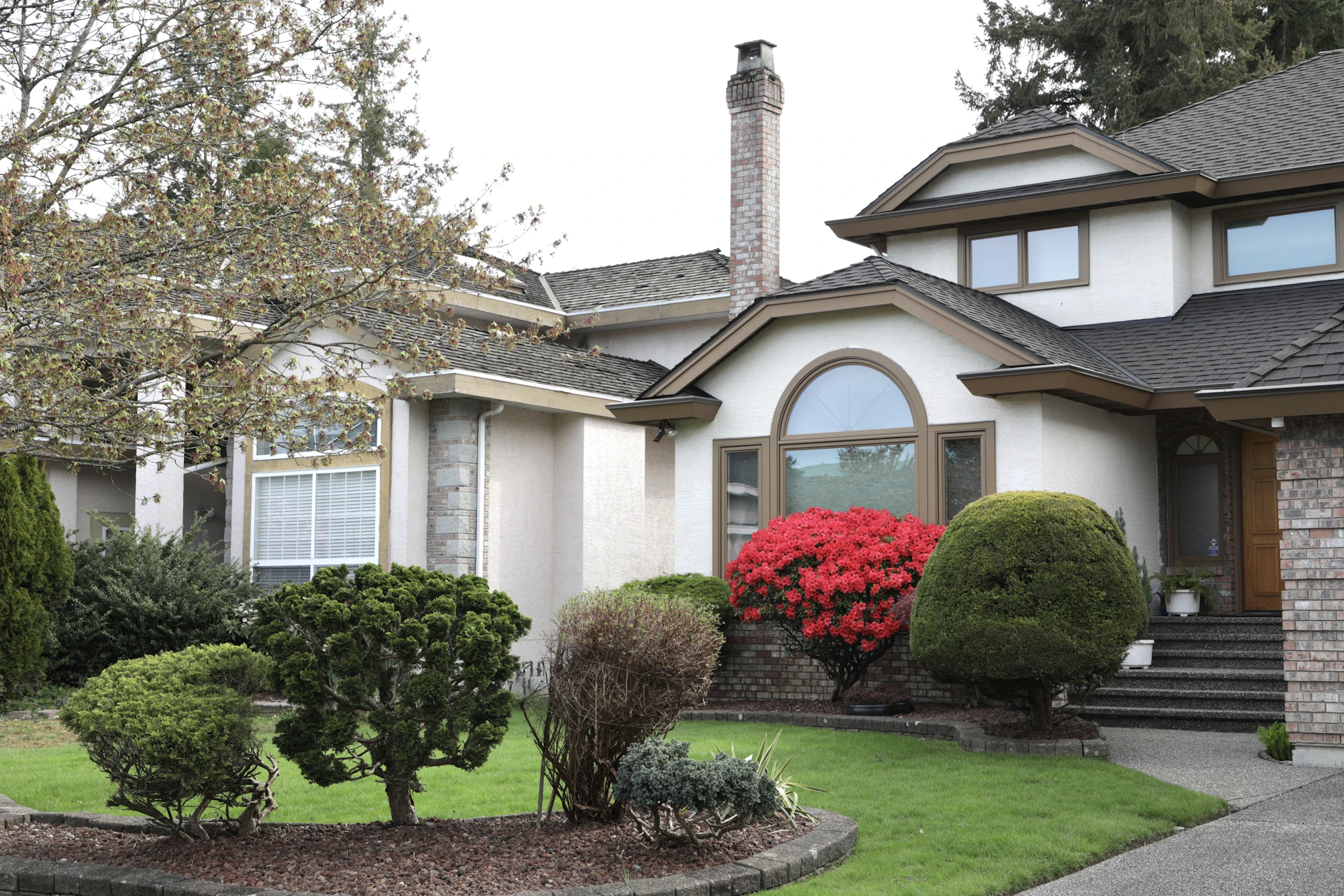 A large house with manicured bushes and red flowers.