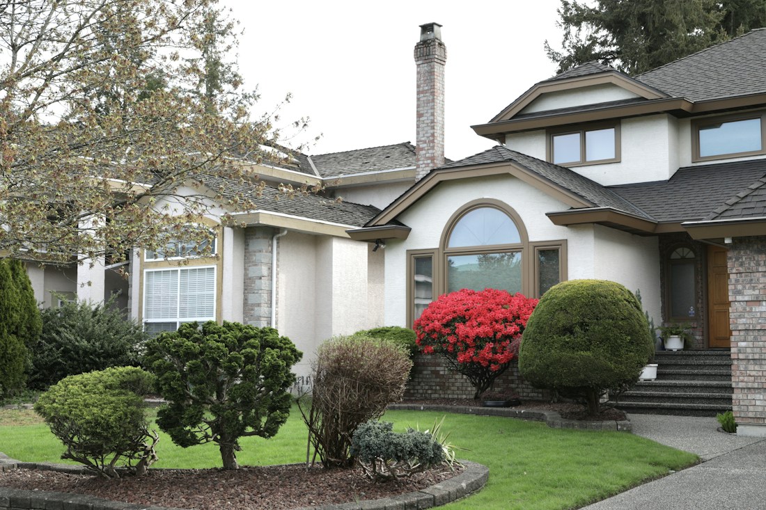 Shingle-style home with clipped shrubs and red azaleas along the front walk