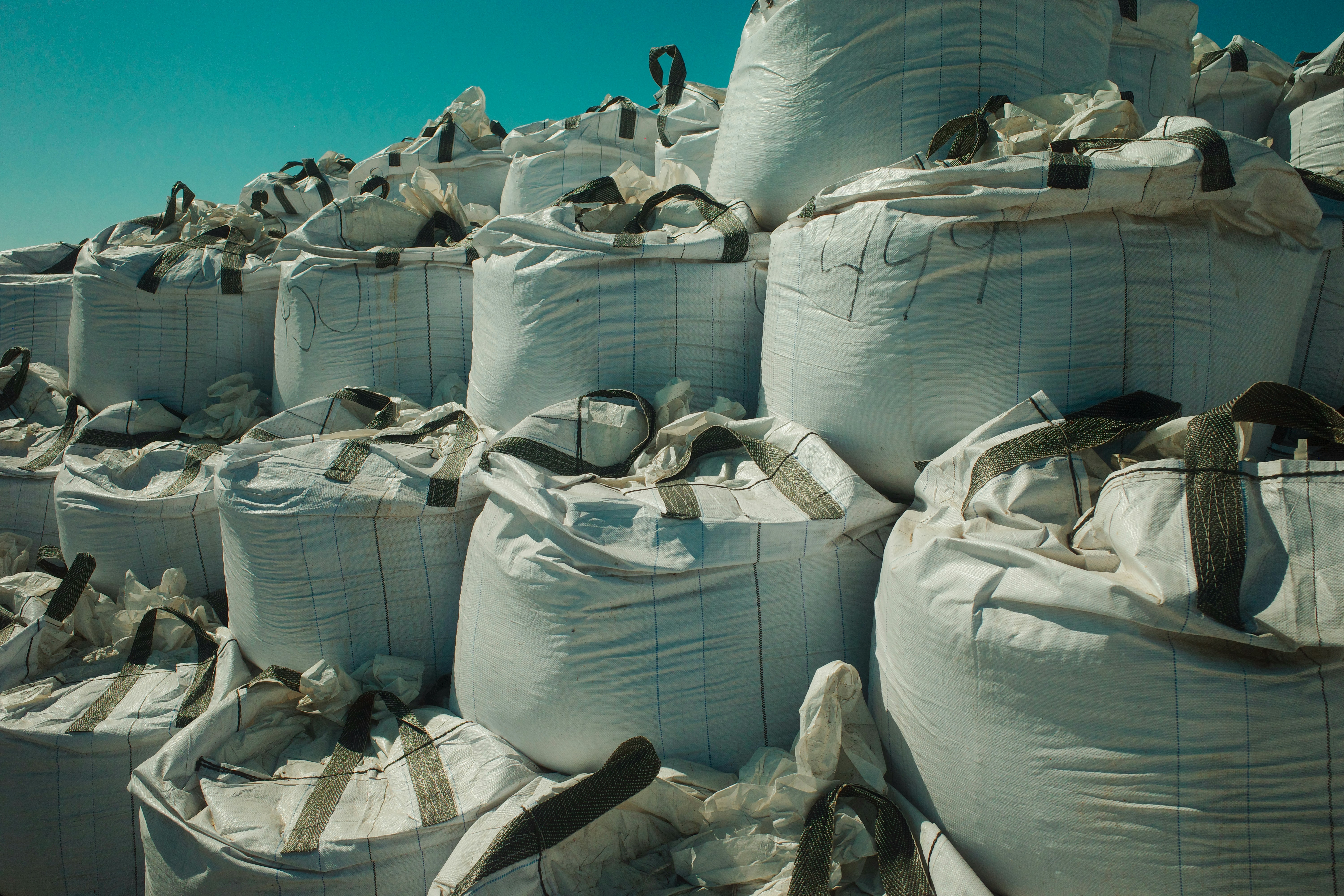 Large white industrial bags stacked outdoors under a clear sky.